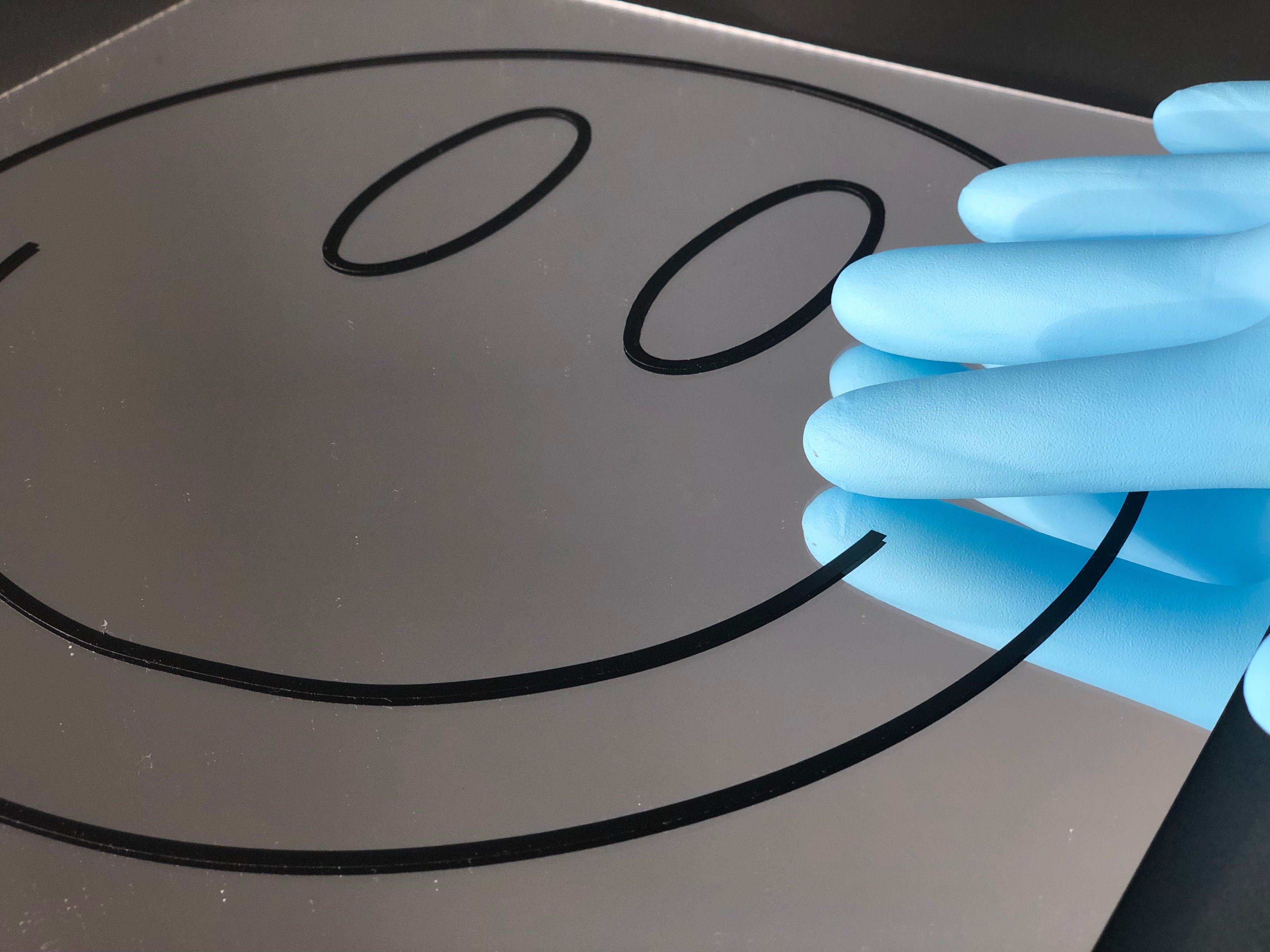 Smiley face graphic on a mirror with a blue-gloved hand