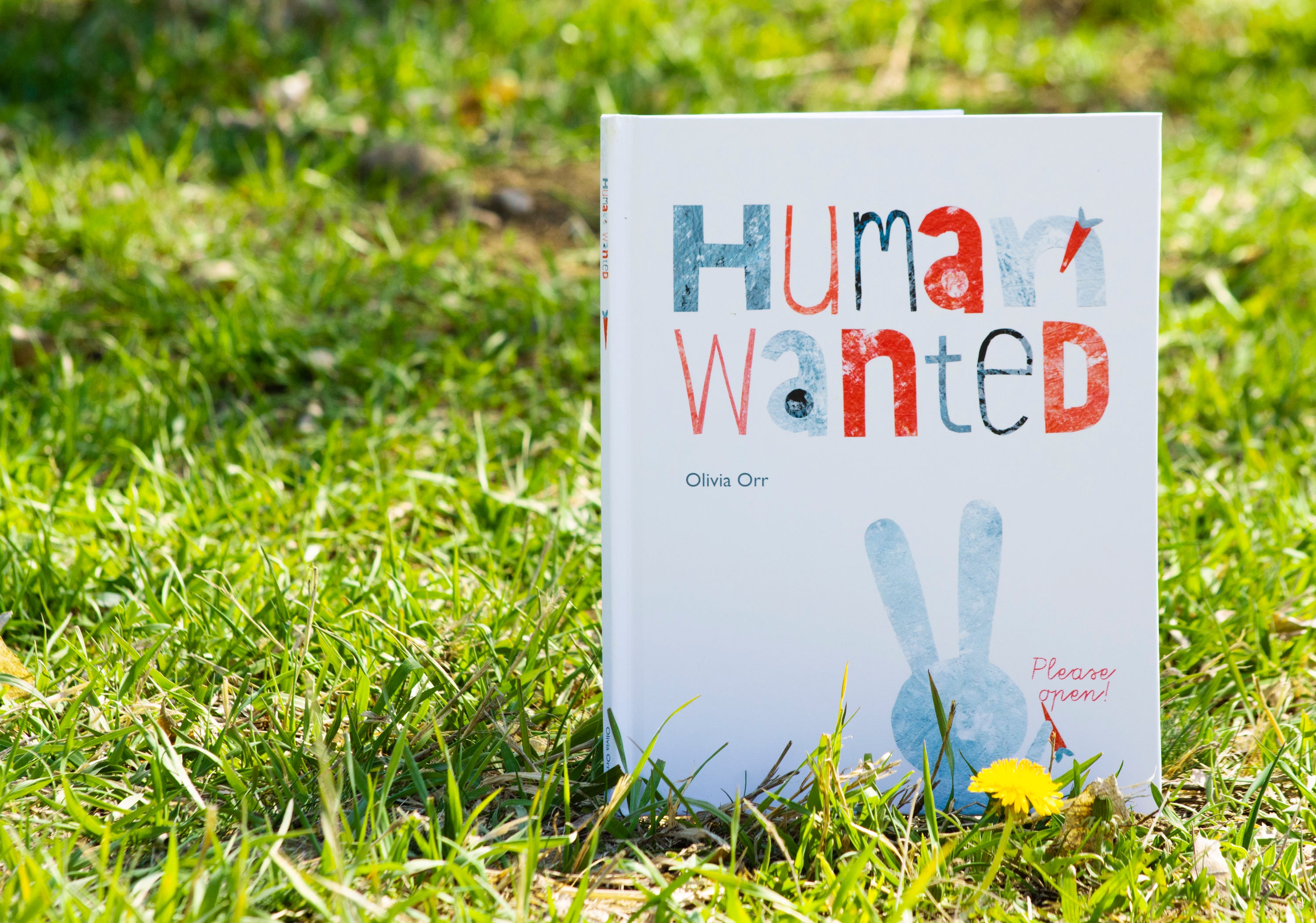 A book titled "Human Wanted" displayed on grass