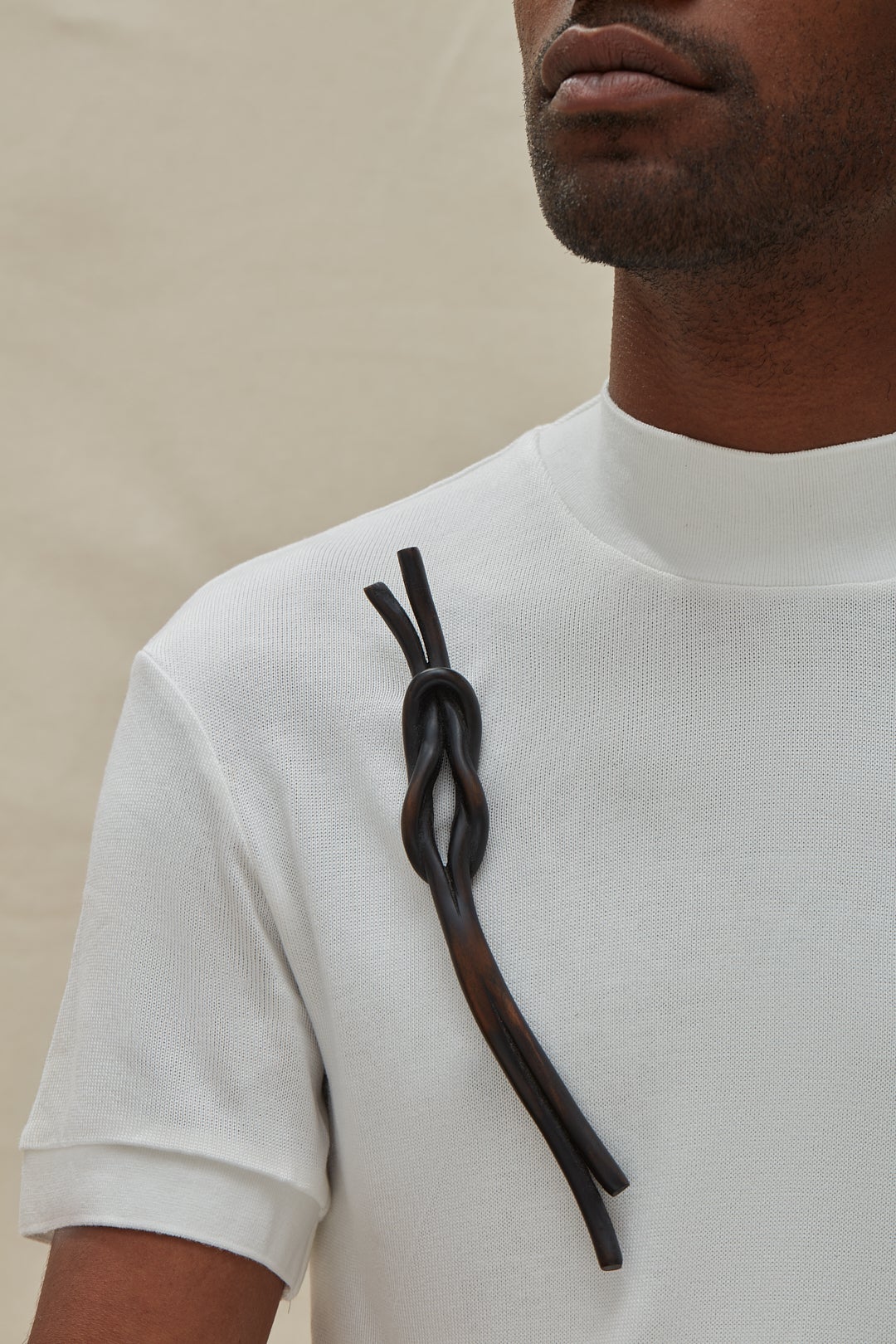 A dark knot brooch carved from wood, worn by a model