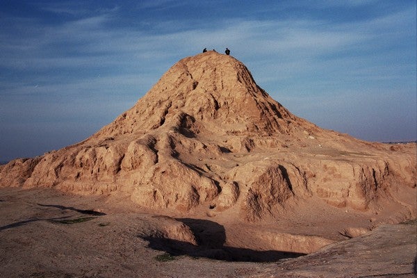/Color%20photograph%20of%20the%20Assur%20Ziggurat.%20What%20is%20left%20of%20the%20ziggurat%20%28it%20is%20mostly%20eroded%29%20rises%20out%20of%20sand%20in%20a%20big%20mound%20against%20a%20blue%20sky.%20There%20are%20three%20small%20figures%20standing%20on%20top.