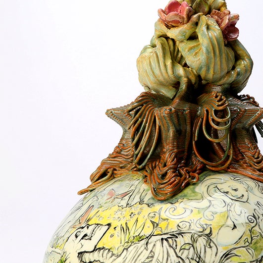 color photo; close up of ceramic object. stylized ceramic sea fauna sit atop a round based that has illustrations of a skeleton and Disney's Ariel
