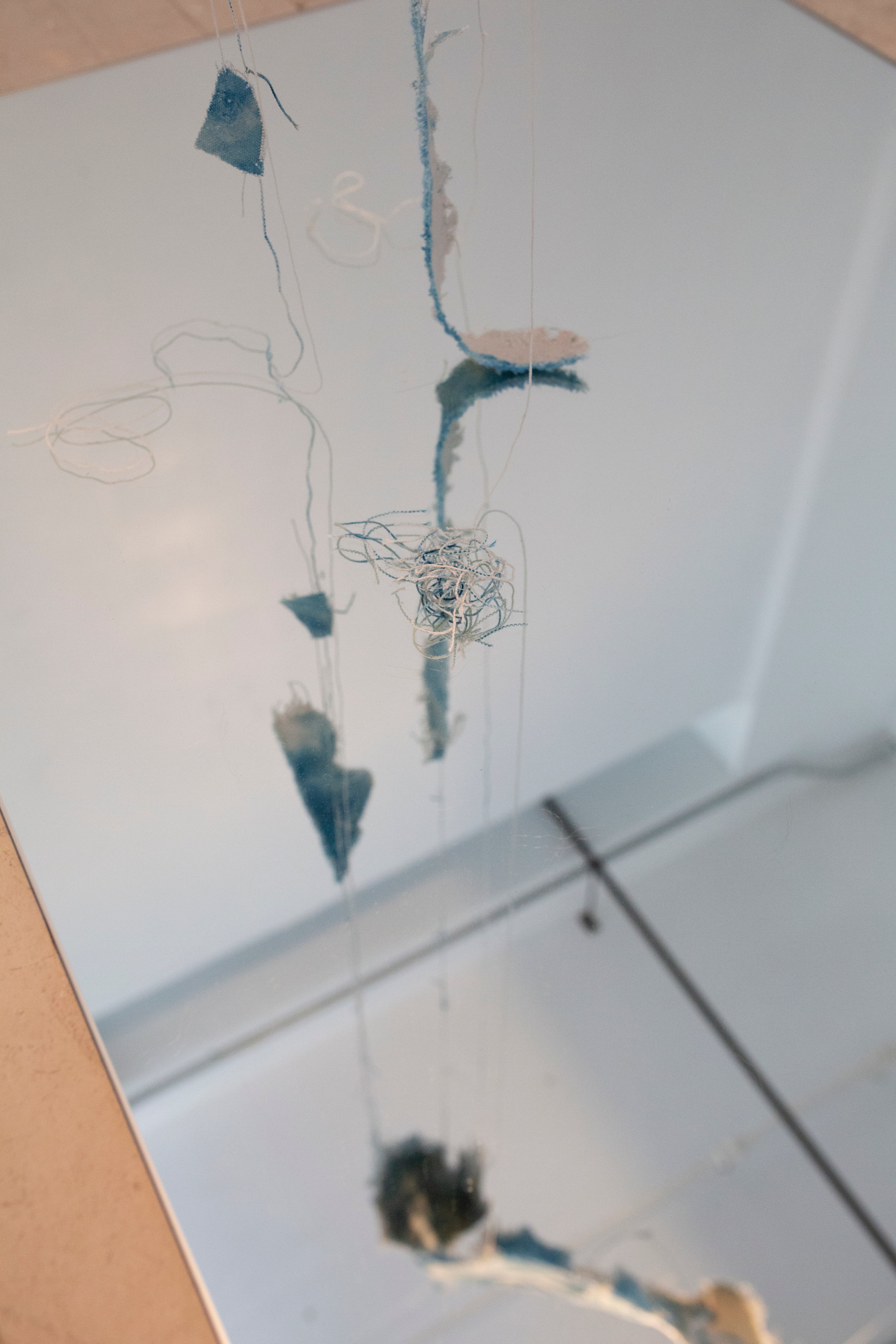 A reflection of beige canvas, dyed with spots of cyanotype is twisted and suspended in the air. The edges of the canvas have been unraveled and hang downward. 