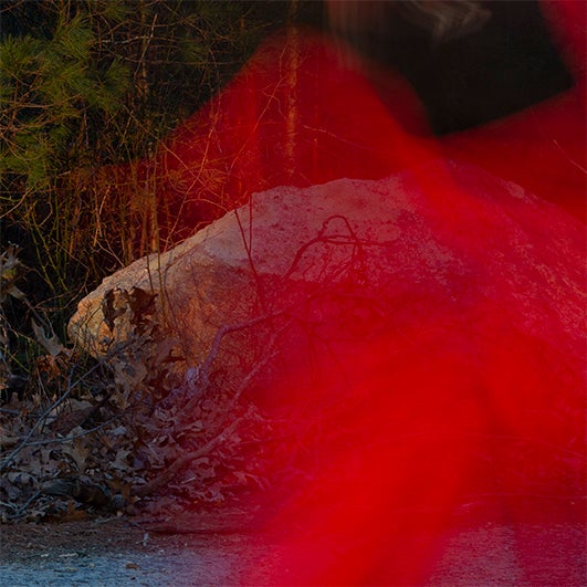 color photo of a large rock in the woods at night. A transparent bright red blur obscures the right side