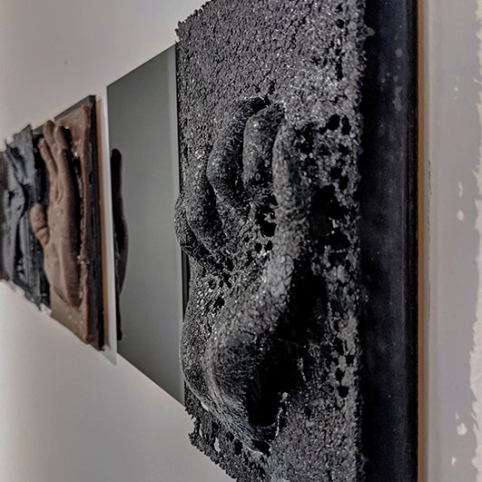 color photograph of a very porous piece of black glass with a fist imprinted into it, as if raised in power or holding something. The photograph is taken from a strong side angle