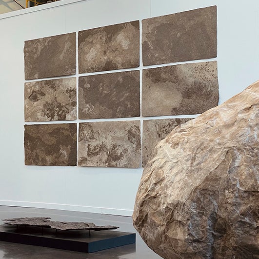 color photograph of a gallery install. There is a 3 by 3 grid of prints which resemble tan lunar landscapes.