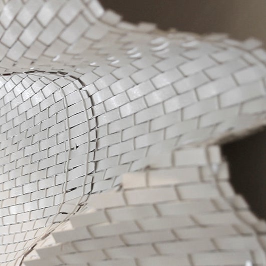 color photograph of a rippling, woven textile piece. It is made of thick strips of a plasticky looking white material