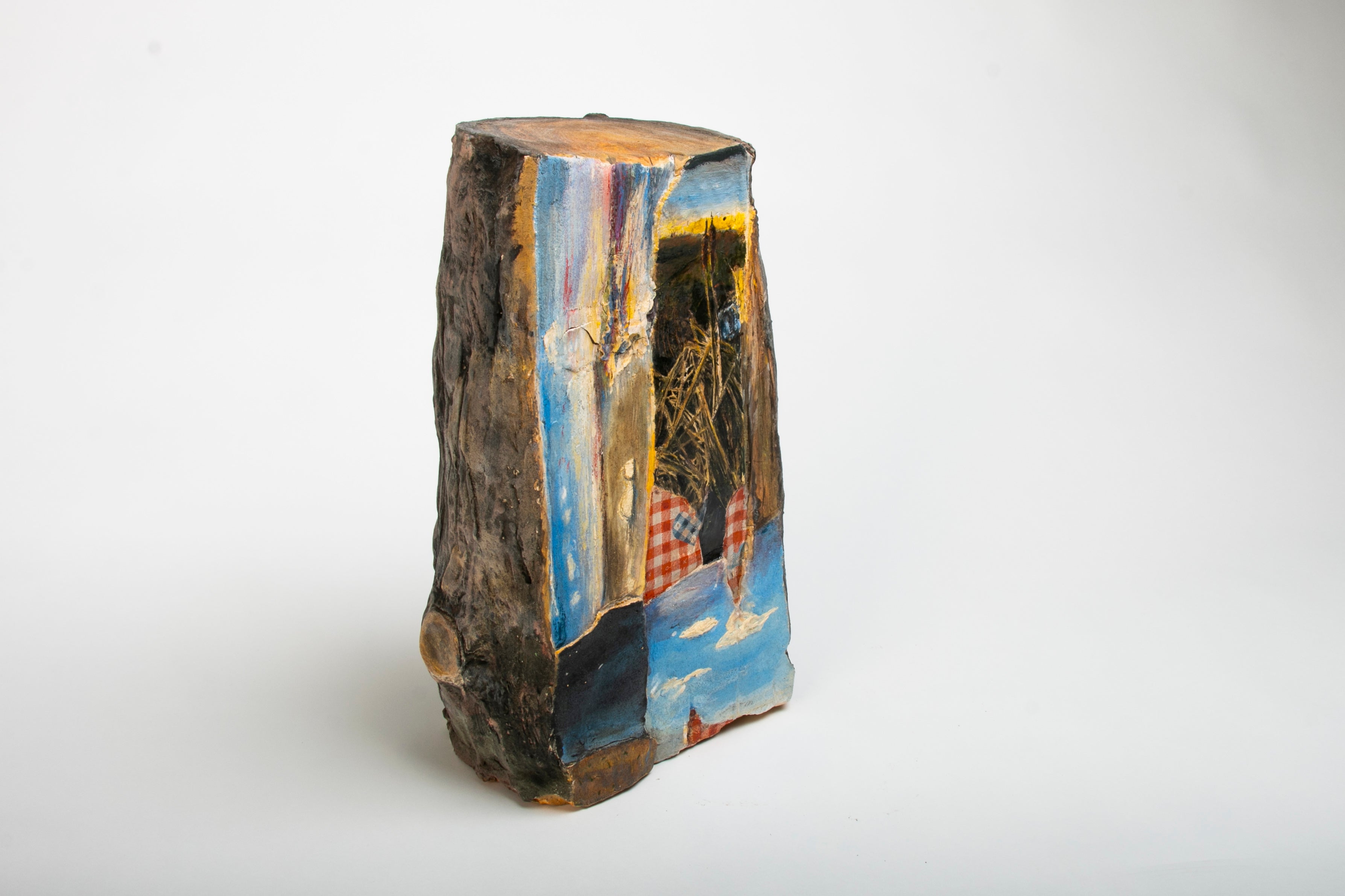 Ceramic piece resembling a cut log. The cut side of log has collaged images of the sea, cattails, and clouds.