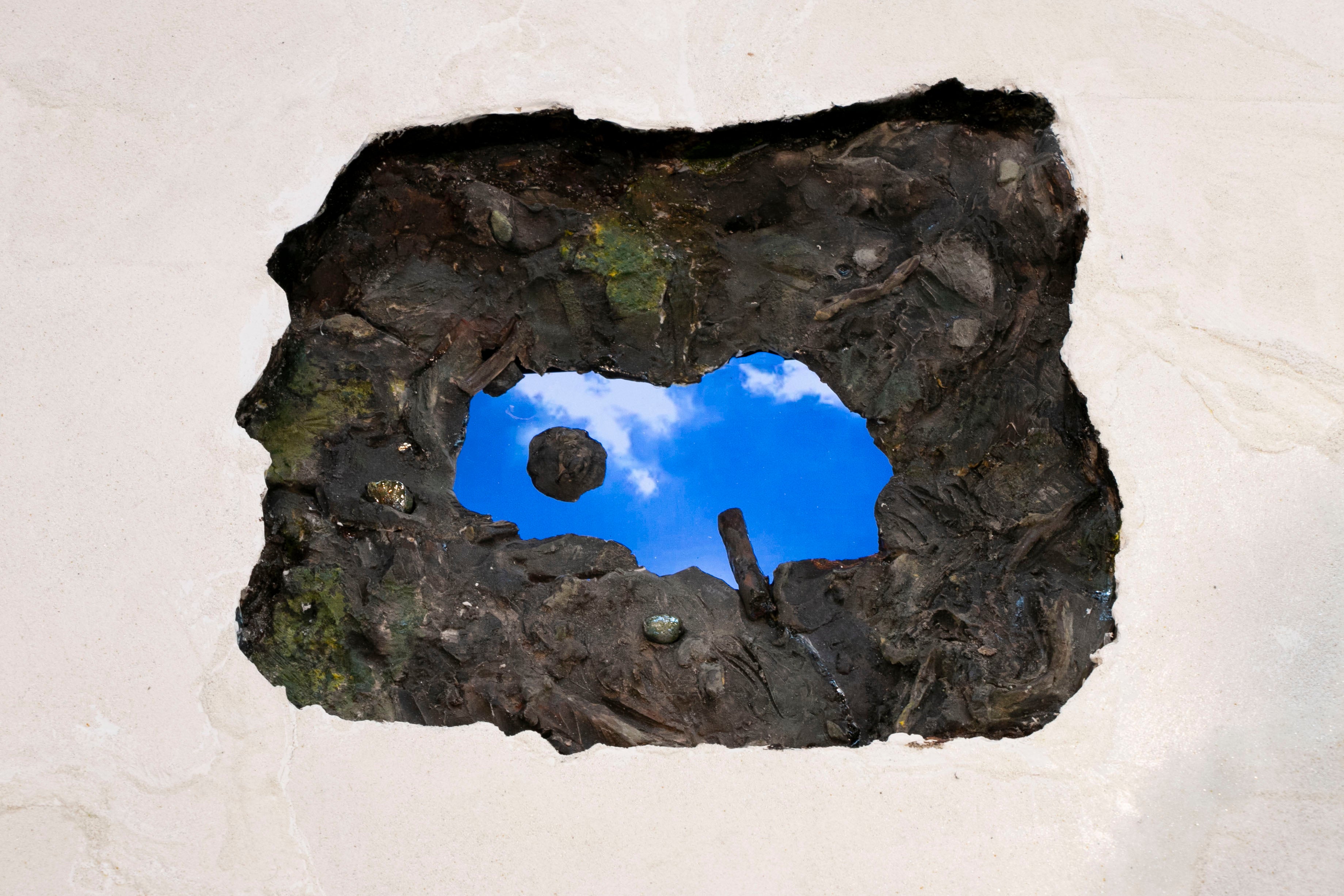 Sculpture of puddle with electronic screen inside playing videos of clouds, cattails  and the artist drawing in sand.