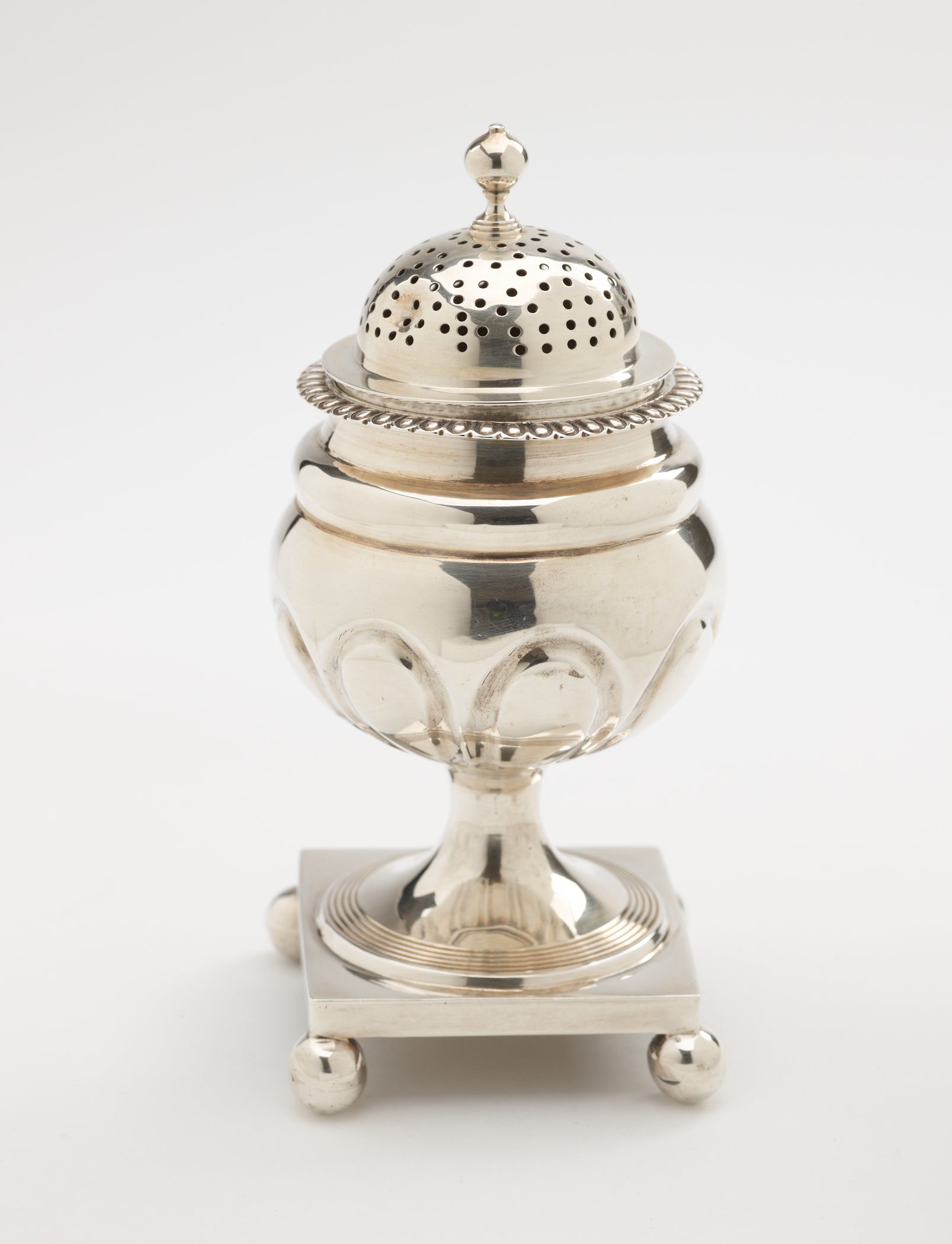 /A%20silver%20caster%20with%20a%20square%20foot%20with%20small%20balls%20in%20each%20corner%2C%20the%20lid%20is%20perforated.%20
