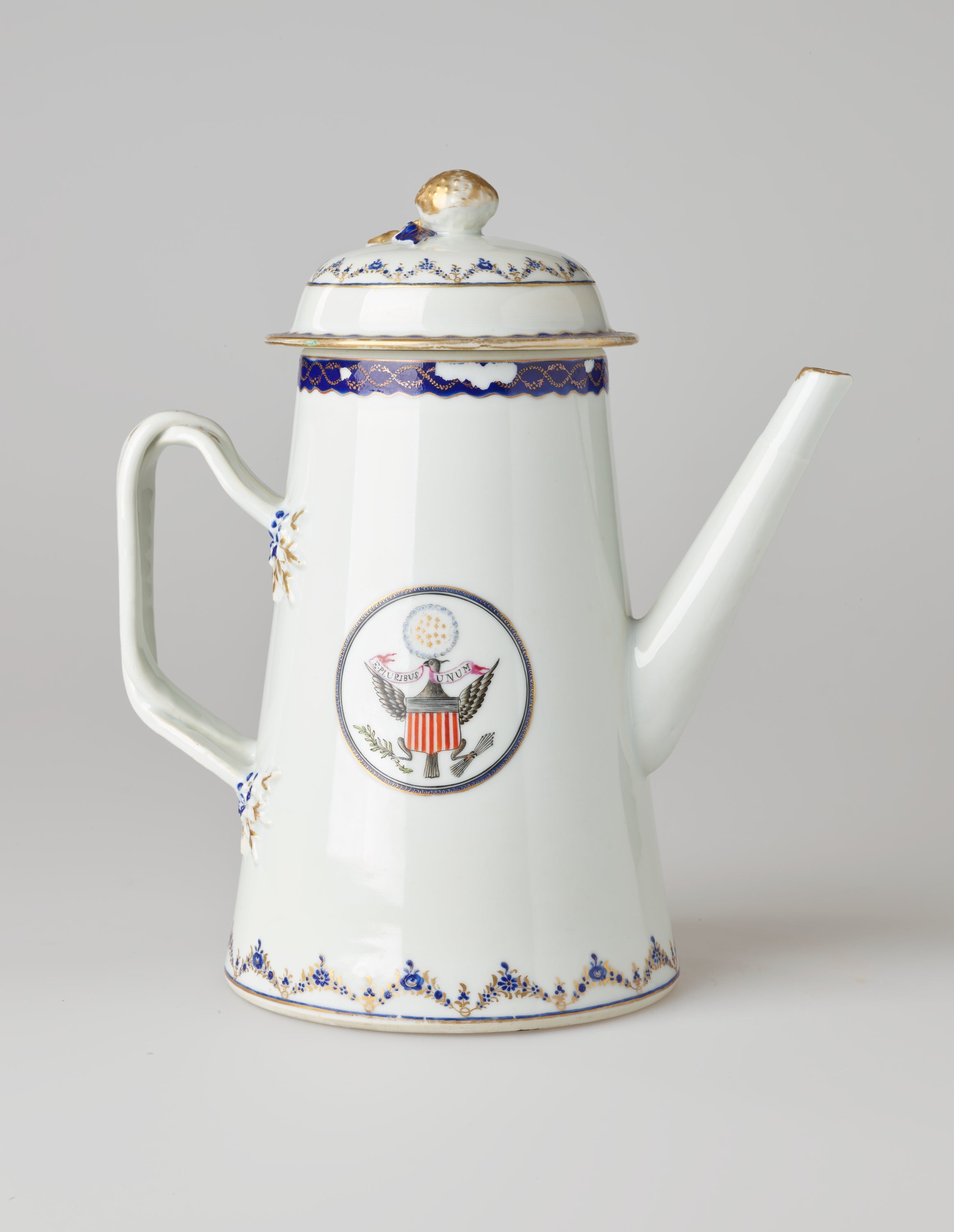 /A%20white%20ceramic%20coffee%20pot%20with%20dark%20blue%20and%20gilded%20decorations%2C%20a%20straight%20spout%2C%20angular%20handle%2C%20and%20heraldry%20imagery%20in%20a%20circle%20on%20the%20body%20of%20the%20coffee%20pot.