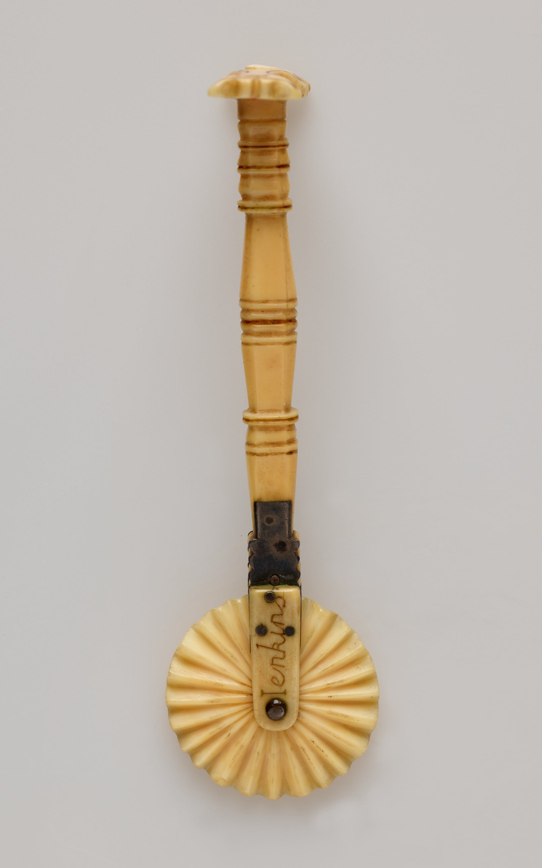 /An%20ivory%20pie%20crimper%20with%20a%20decorative%20handle%20and%20a%20textured%20wheel.%20There%20are%20letters%20on%20the%20part%20attaching%20the%20wheel%20to%20the%20handle.
