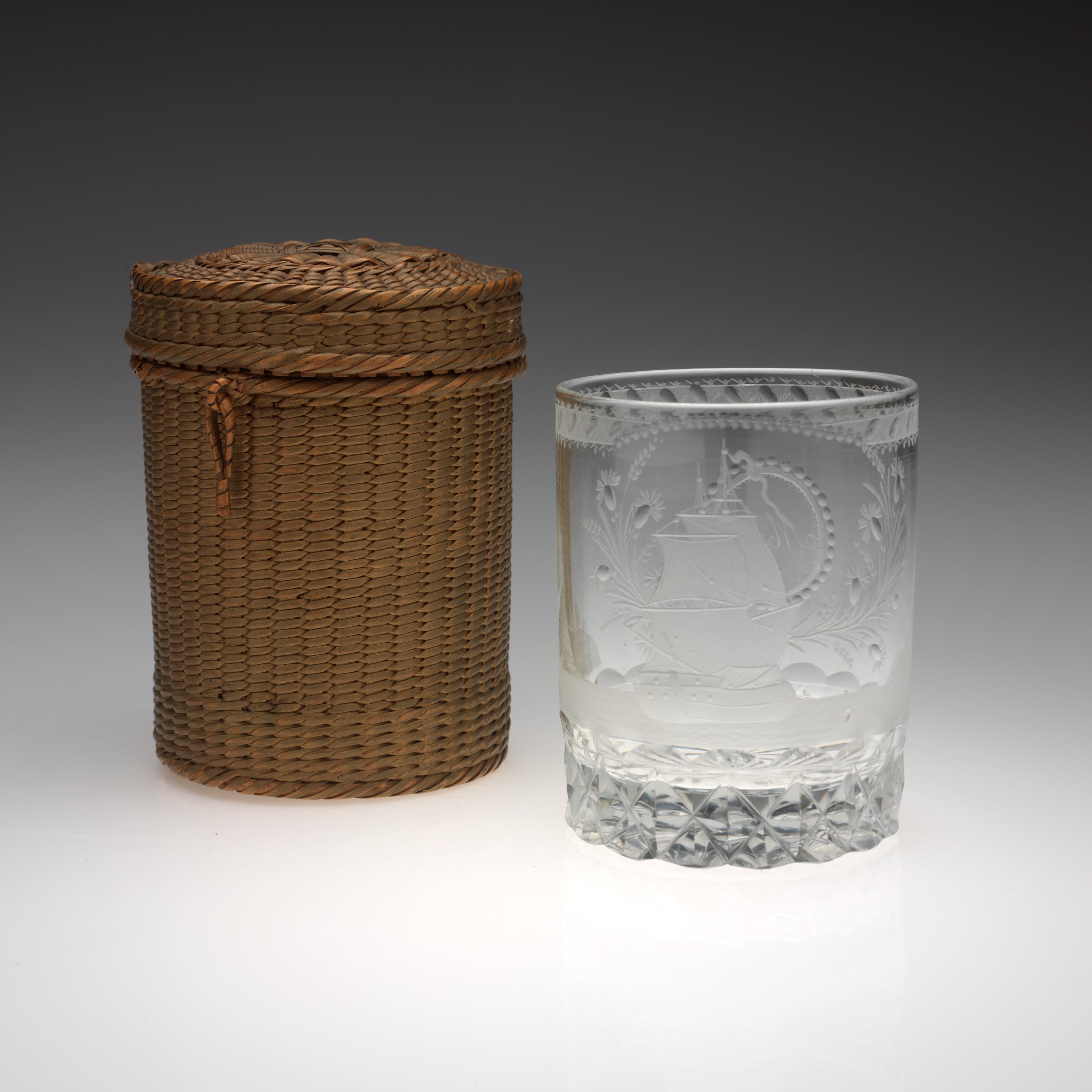 /Rounded%20clear%20glass%20with%20etched%20designs%20next%20to%20a%20brown%20woven%20basket%20of%20the%20same%20shape.%20A%20small%2C%20tan-colored%20implement%20lays%20to%20the%20left%20of%20the%20basket%20and%20glass.%20