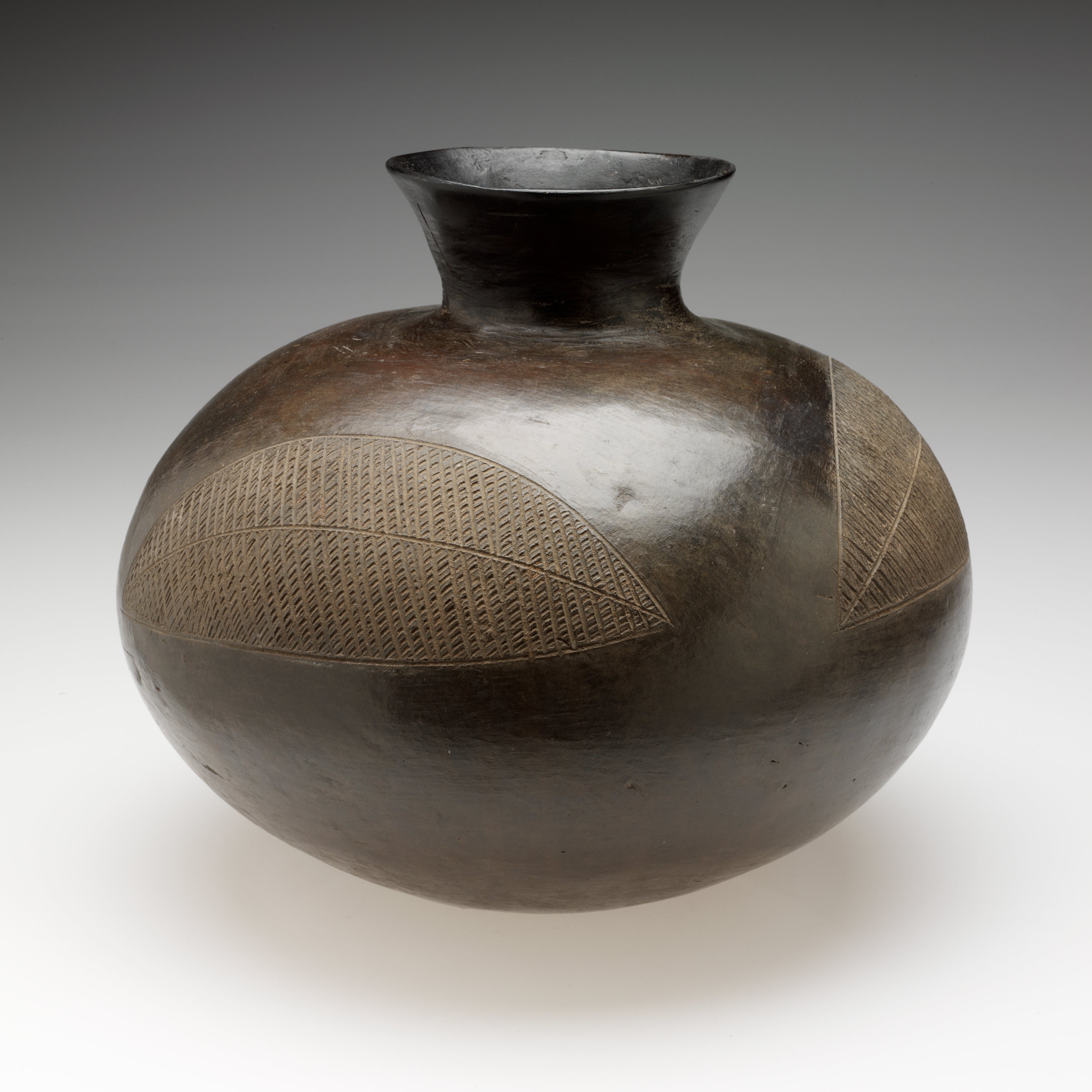 /A%20bulbous%20vessel%20with%20a%20rounded%2C%20flared%20neck.%20Two%20large%2C%20abstract%20leaf-shaped%20designs%20are%20scratched%20into%20the%20shiny%20surface.%20