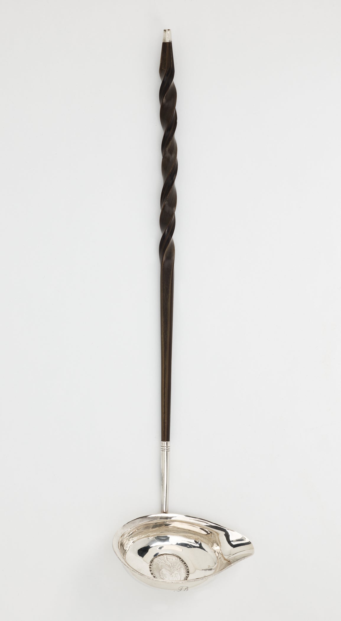 /A%20silver%20and%20baleen%20coin%20ladle.%20The%20handle%20is%20twisted%20and%20dark%20and%20the%20ladle%20is%20silver%20with%20a%20small%20coin%20in%20the%20center.%20