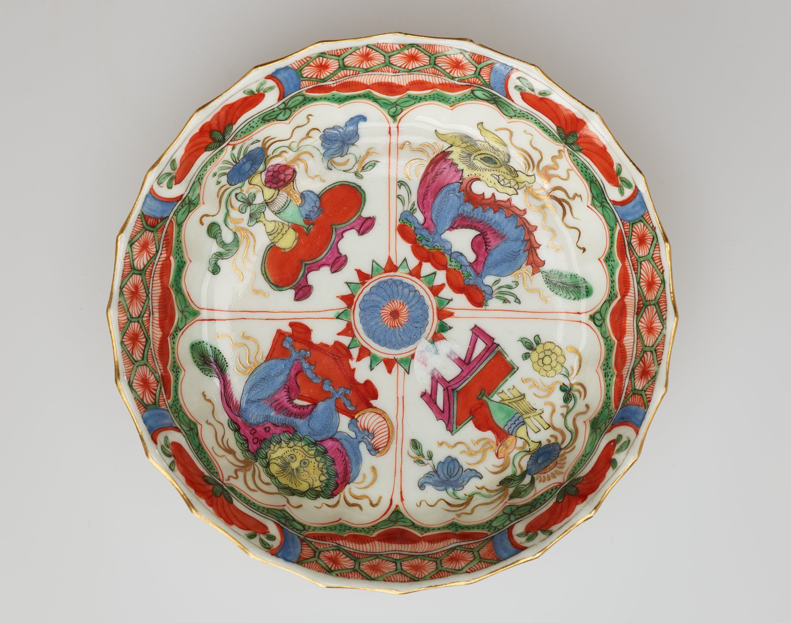 /A%20white%20saucer%20with%20green%2C%20red%2C%20blue%2C%20pink%2C%20yellow%2C%20and%20gilded%20decorations.%20Decorations%20separated%20into%20four%20vignettes%3B%20two%20animals%20and%20two%20scenes%20of%20a%20table%20and%20vessels%20containing%20floral%20elements.