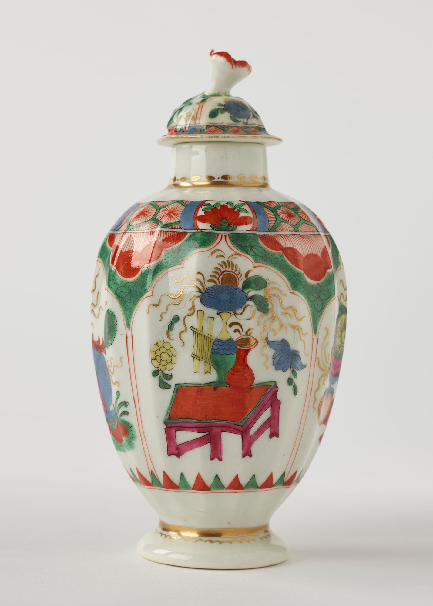 /A%20porcelain%20tea%20caddy%20with%20a%20lid%20and%20green%2C%20red%2C%20blue%2C%20pink%2C%20yellow%20and%20gilded%20decorations.%20The%20finial%20is%20a%20sculptural%20flower%20white%2C%20red%20and%20green
