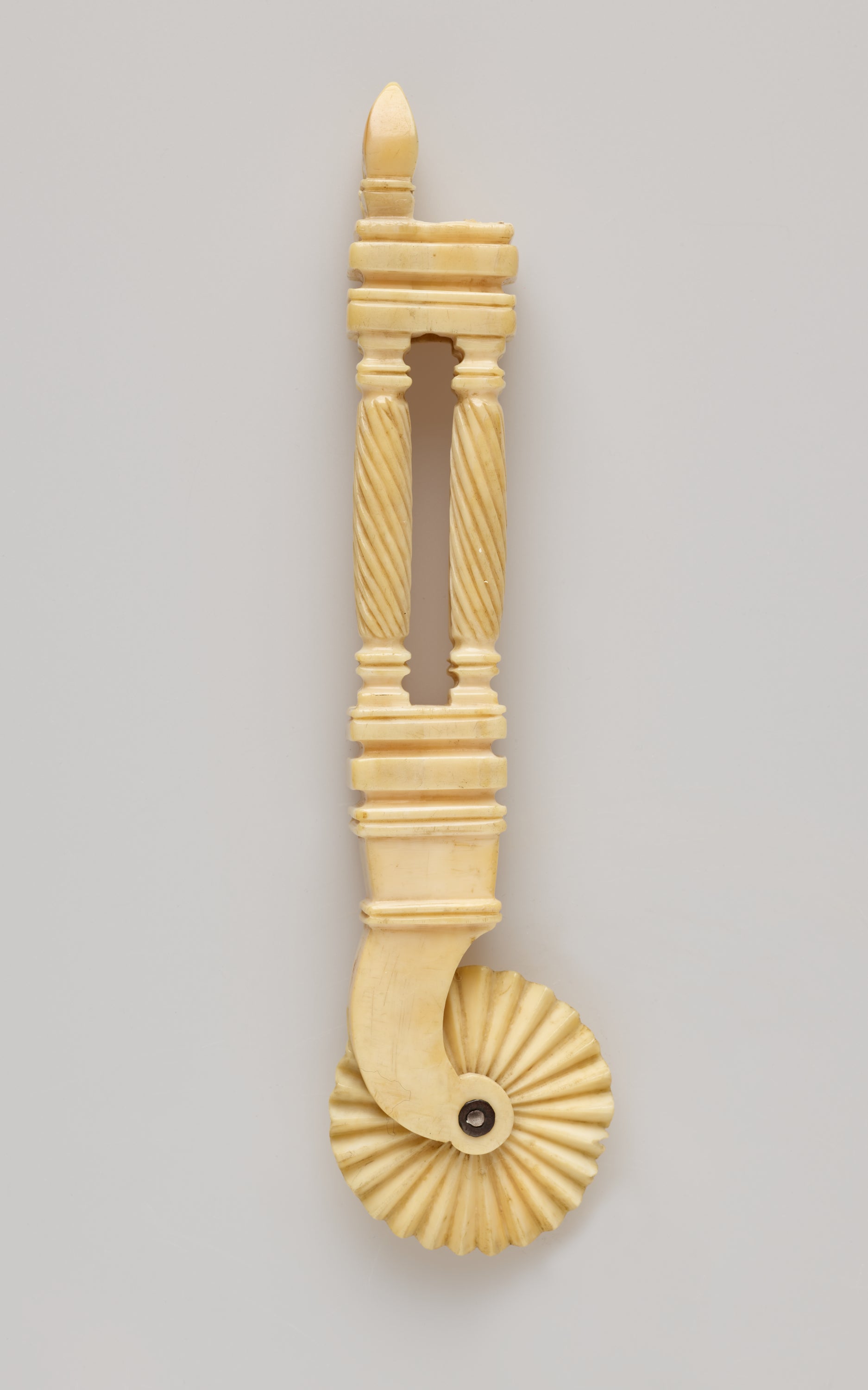 /An%20ivory%20pie%20crimper%20with%20a%20decorative%20handle%20and%20a%20textured%20wheel.%20The%20handle%20has%20a%20cutout%20in%20the%20middle%20of%20it.