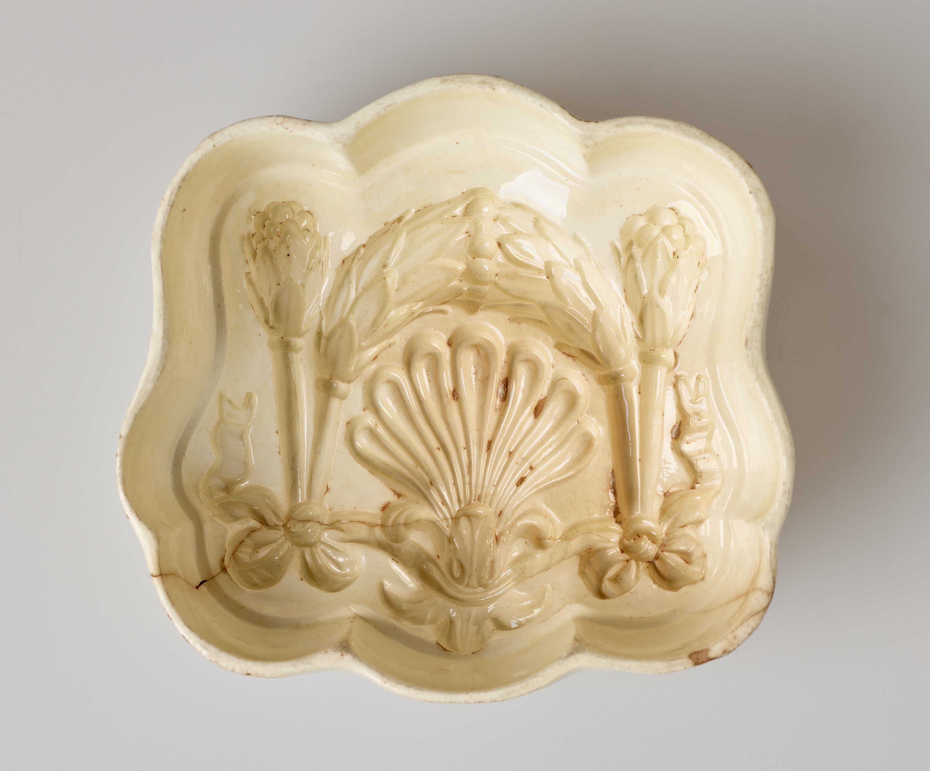/A%20ceramic%20pudding%20mould%20that%20is%20cream%20colored%20and%20is%20curved%20with%20inset%20floral%20and%20bow%20decorations.
