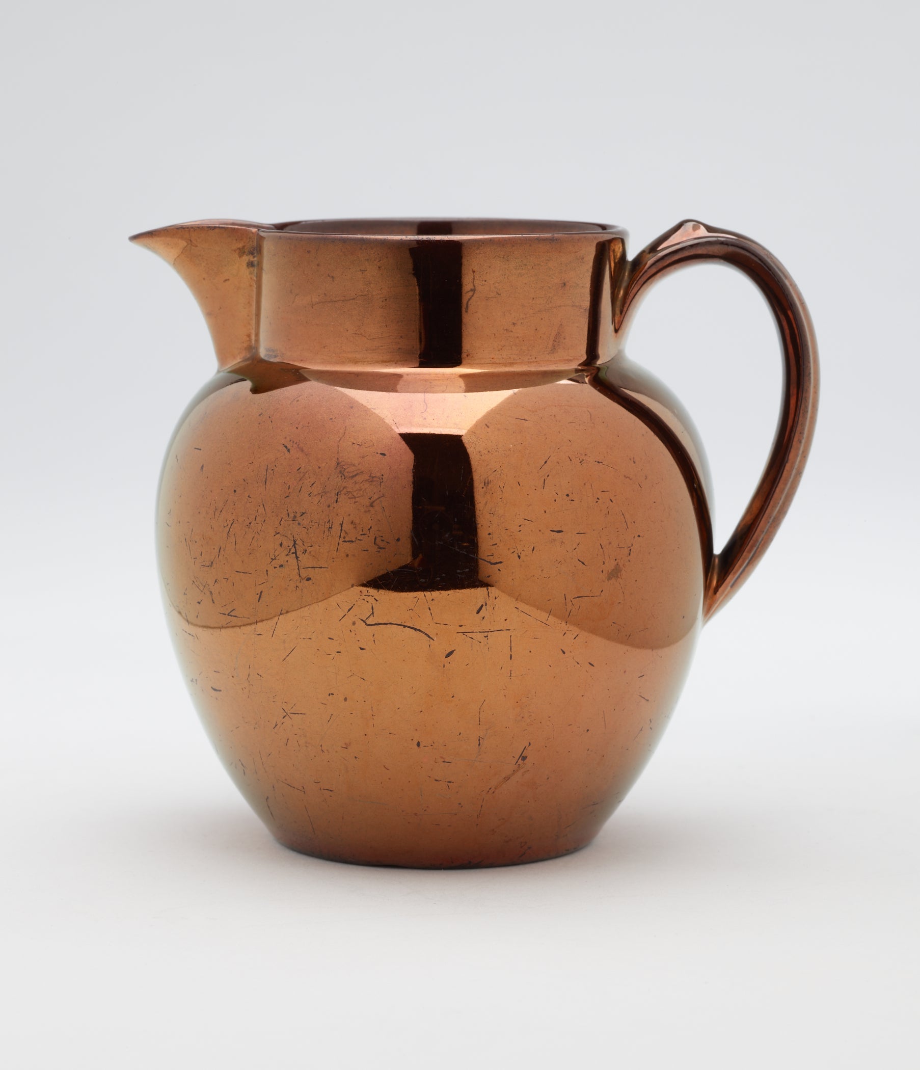 /A%20ceramic%20jug%20with%20a%20small%20handle.%20The%20glaze%20is%20a%20brown%20metallic%20color.