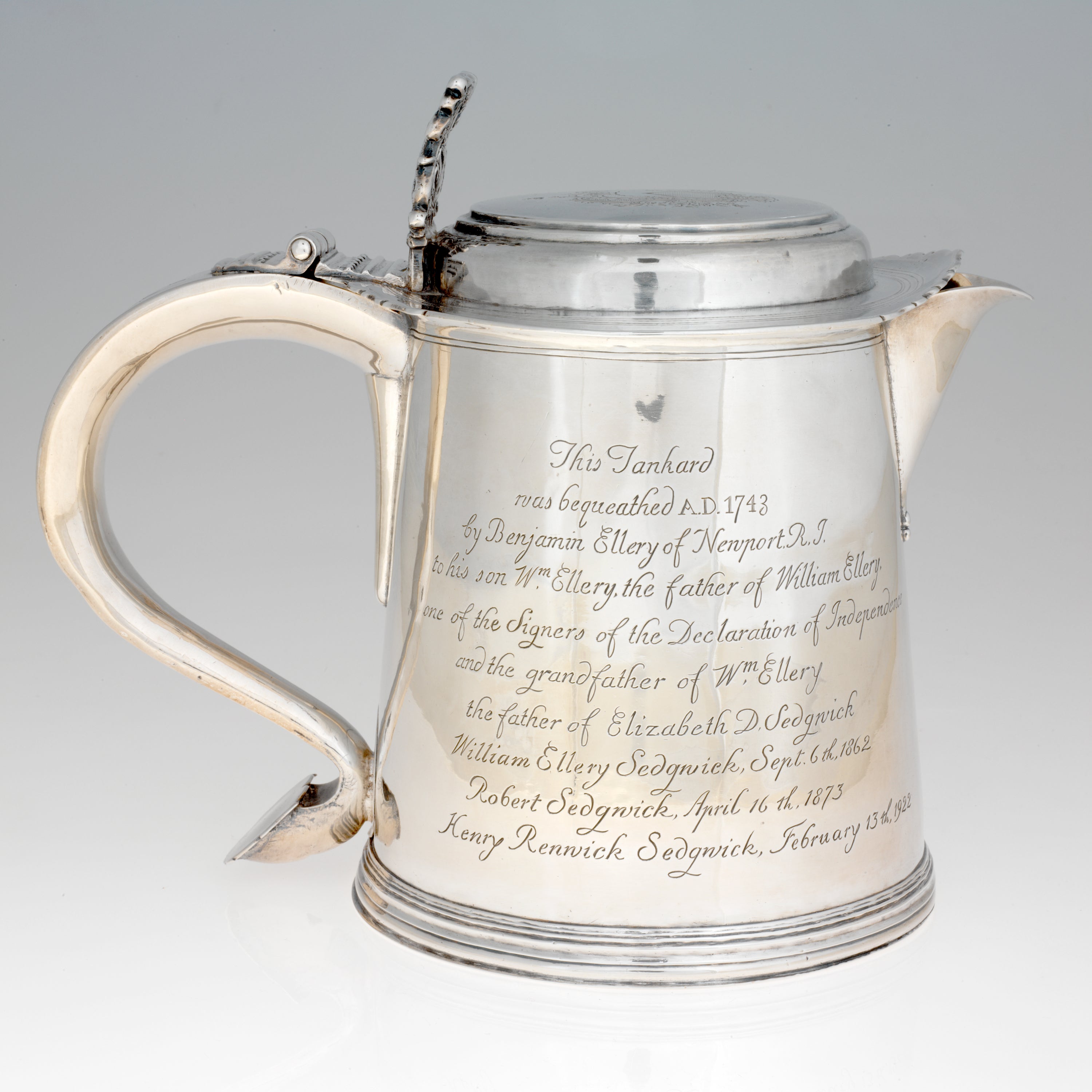 /A%20rounded%20silver%20vessel%20with%20a%20curved%20handle%2C%20lid%2C%20and%20spout.%20Side%20of%20the%20vessel%20is%20covered%20with%20engraved%20writing.%20