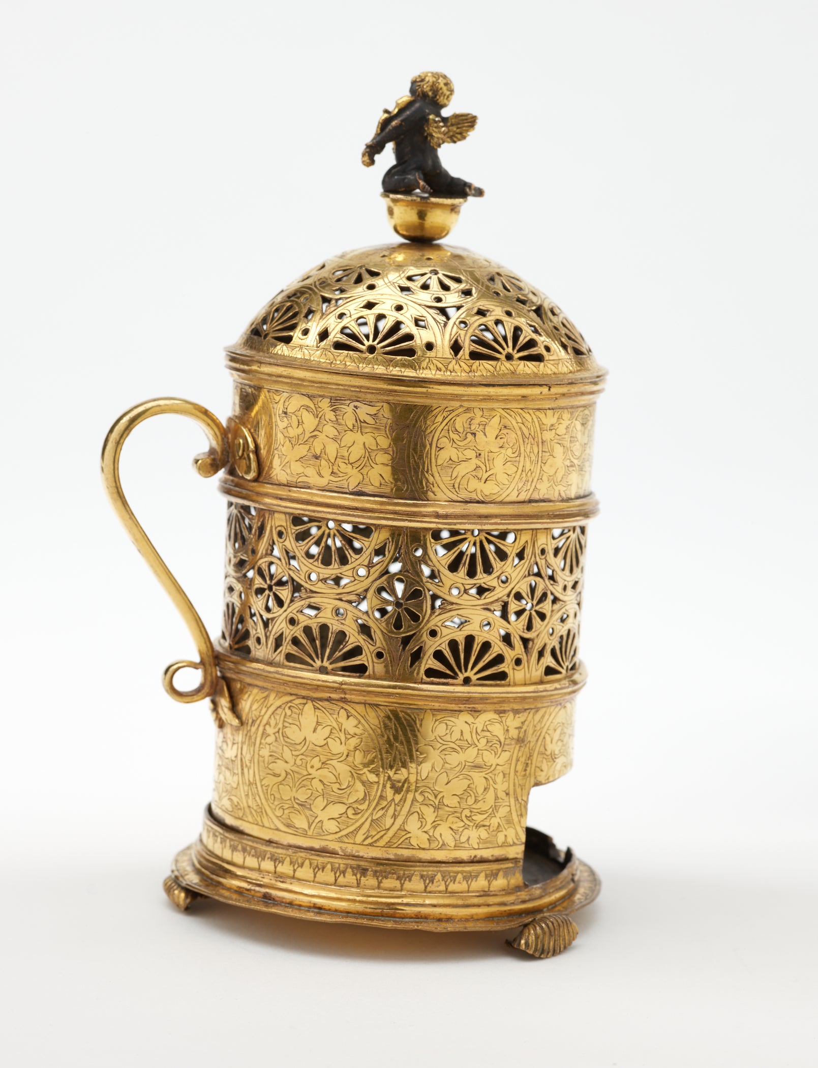 /Gold%20colored%20pierced%20vessel%20with%20handle.%20Small%20dark%20figure%20sits%20on%20top.