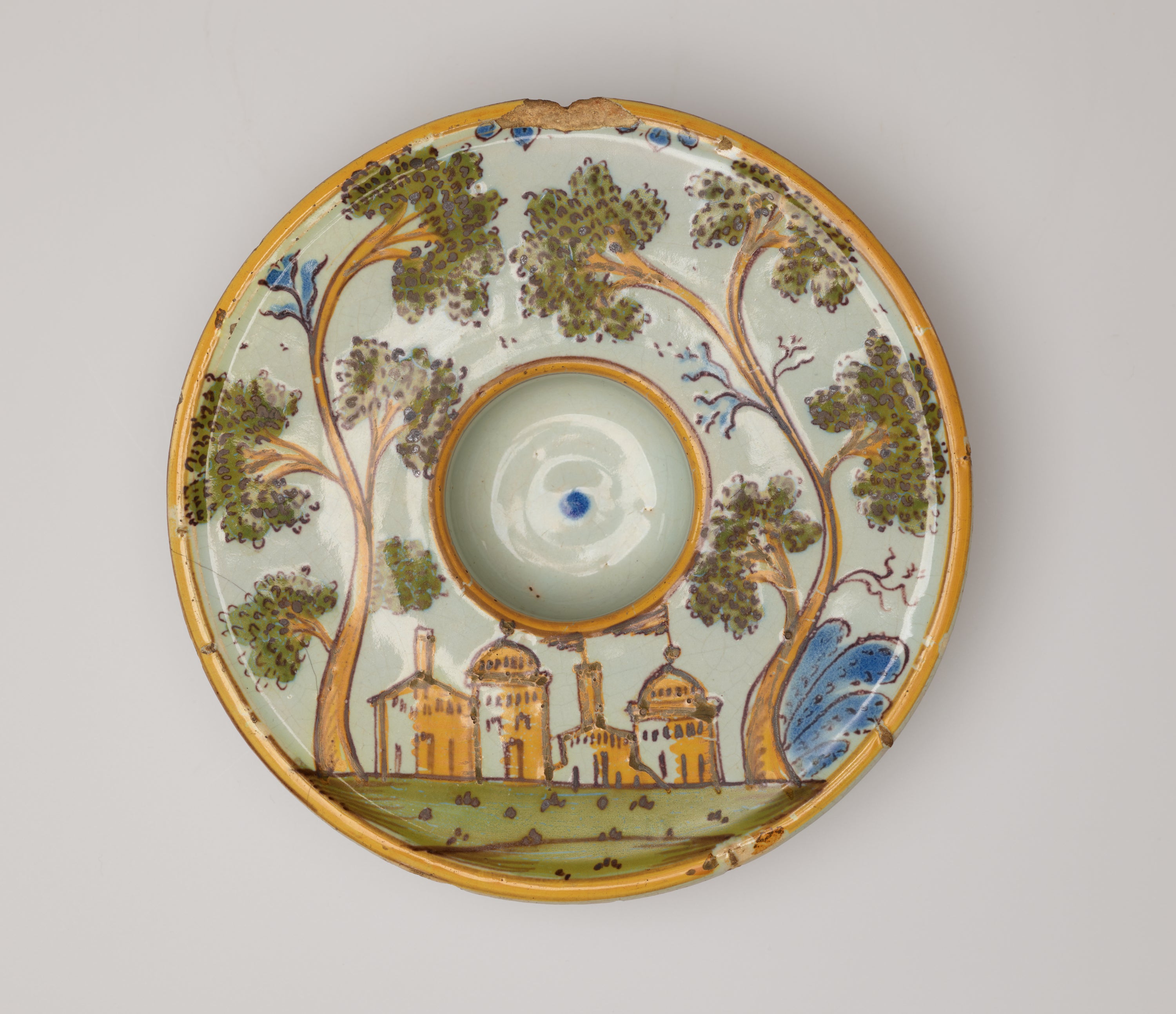 /Round%20plate%20decorated%20with%20an%20image%20of%20buildings%20and%20trees.%20There%20is%20a%20concave%20well%20in%20the%20center%20of%20the%20form.%20