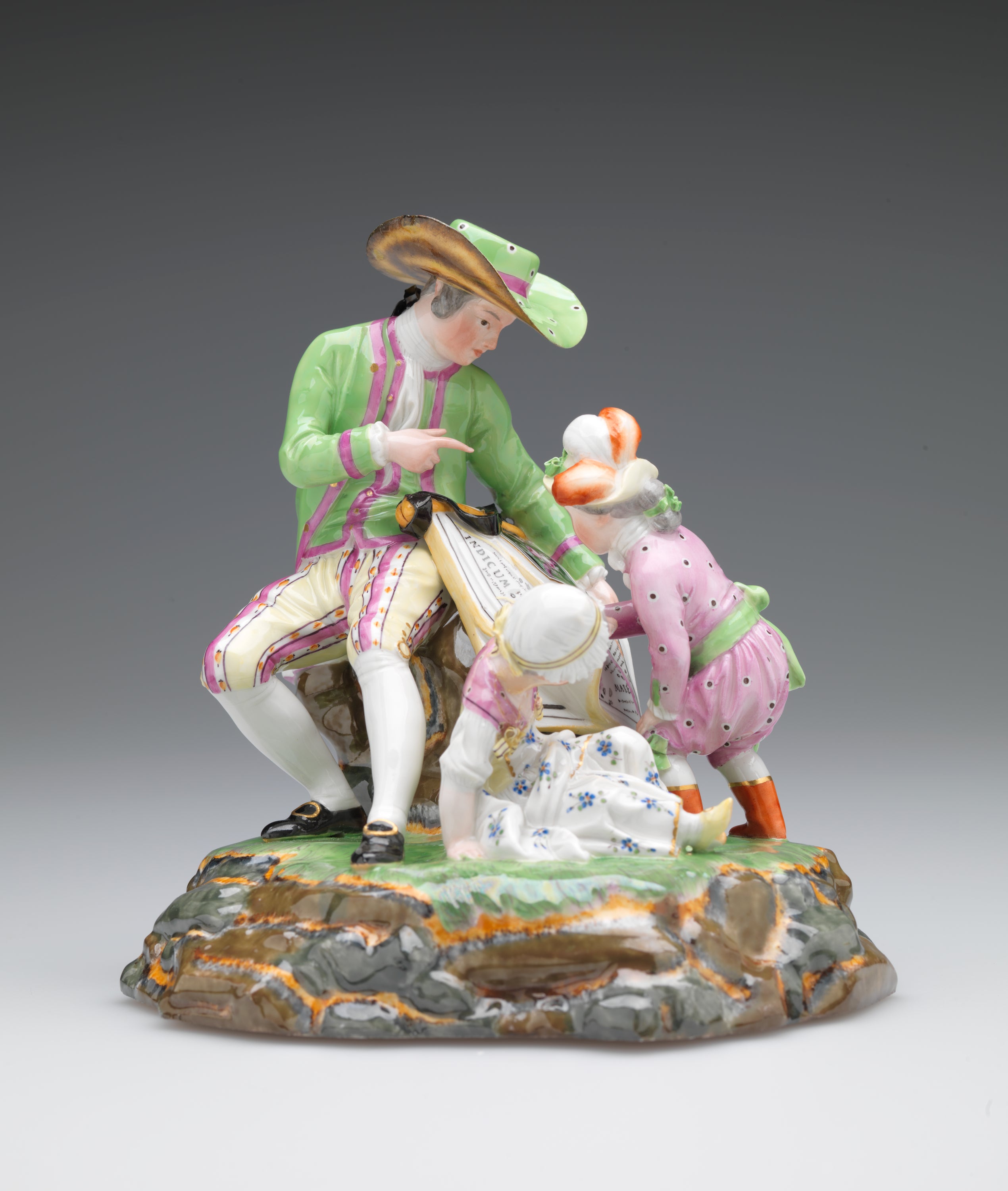 /A%20sculpture%20with%20three%20figures%20in%20elaborate%20historical%20clothing.%20A%20seated%20light-skinned%20figure%20holds%20a%20roll%20of%20maps%20while%20one%20child%20examines.%20A%20second%20child%20sits%20near%20them.
