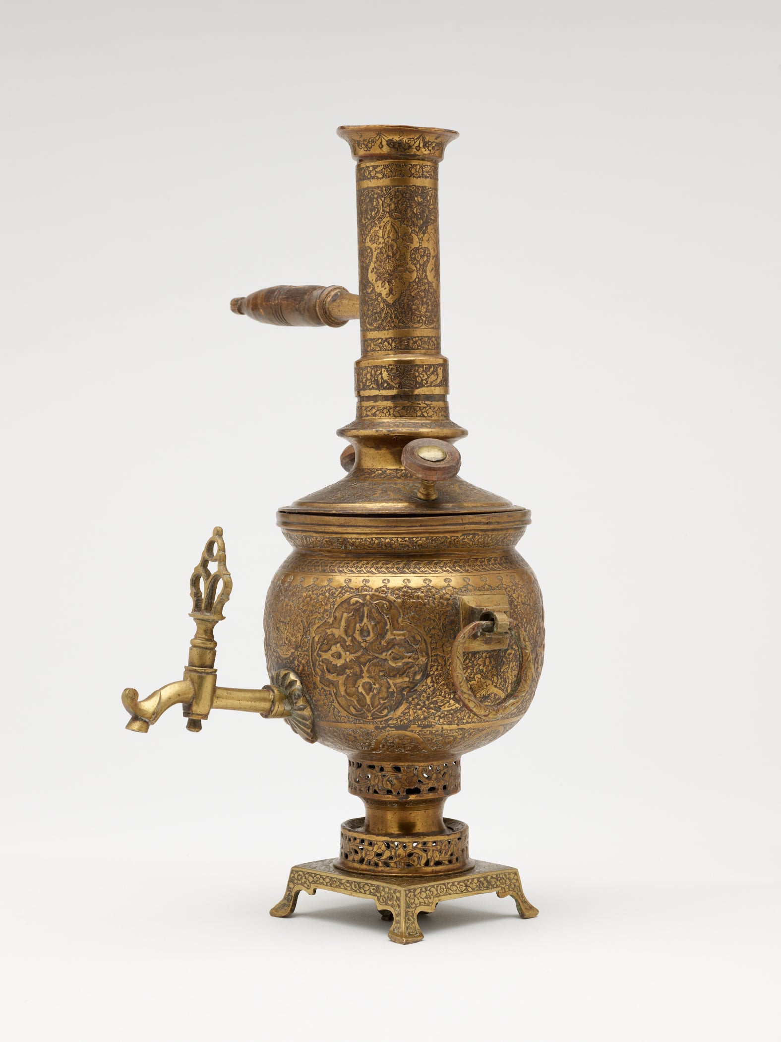 /A%20brass%20and%20wood%20tea%20instrument%20that%20has%20a%20decorative%20foot%2C%20lid%2C%20various%20handles%20and%20rings%2C%20and%20spout.%20The%20entire%20vessel%20has%20highly%20decorative%20engravings.%20
