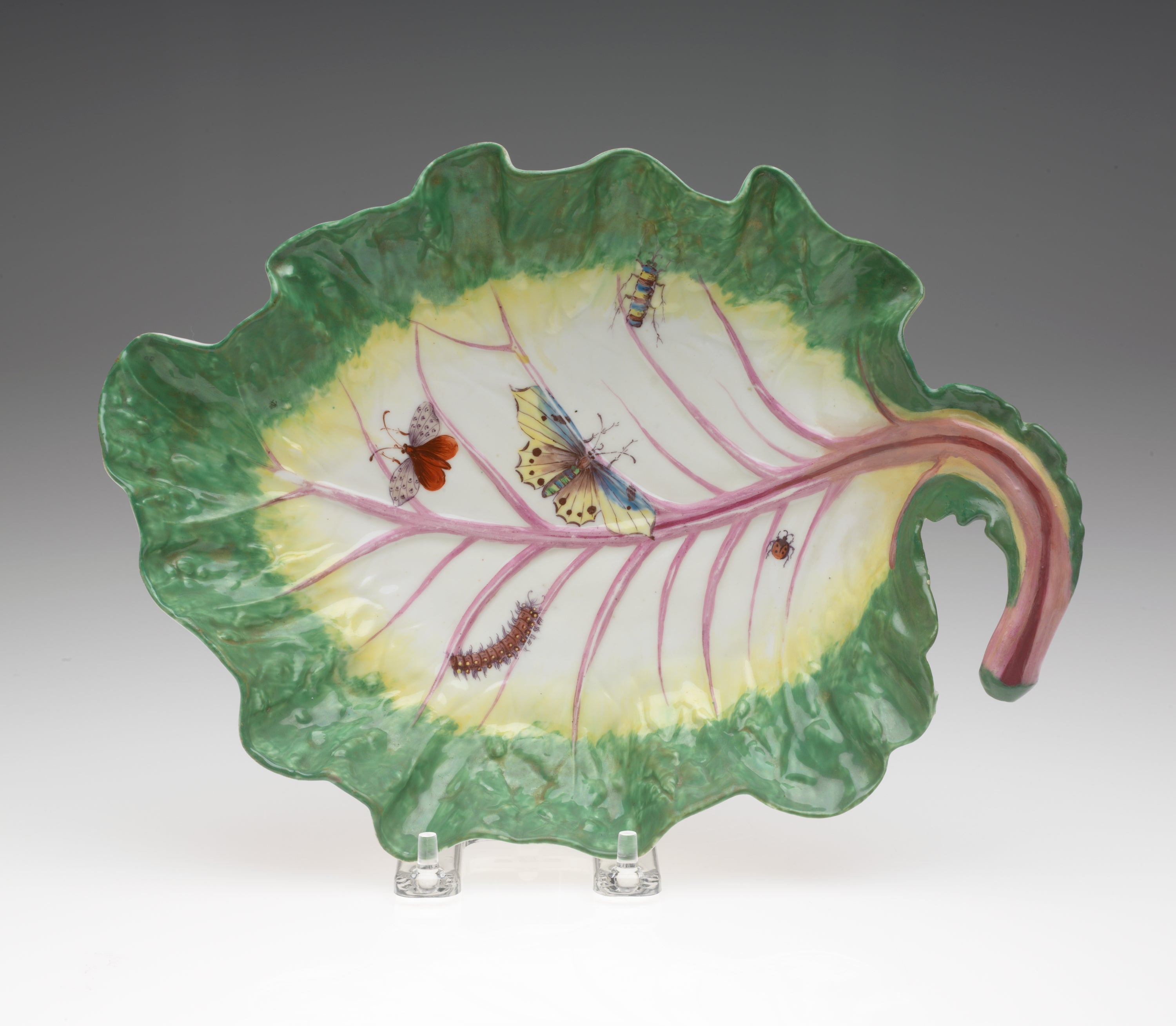 /A%20leaf%20shaped%20porcelain%20dish%2C%20green%20on%20the%20edge%20to%20yellow%20then%20white%2C%20the%20stem%20is%20pink%2C%20with%20five%20insects%20depicted%3A%20a%20lady%20bug%2C%20two%20butterflies%2C%20a%20caterpillar%2C%20and%20beetle.