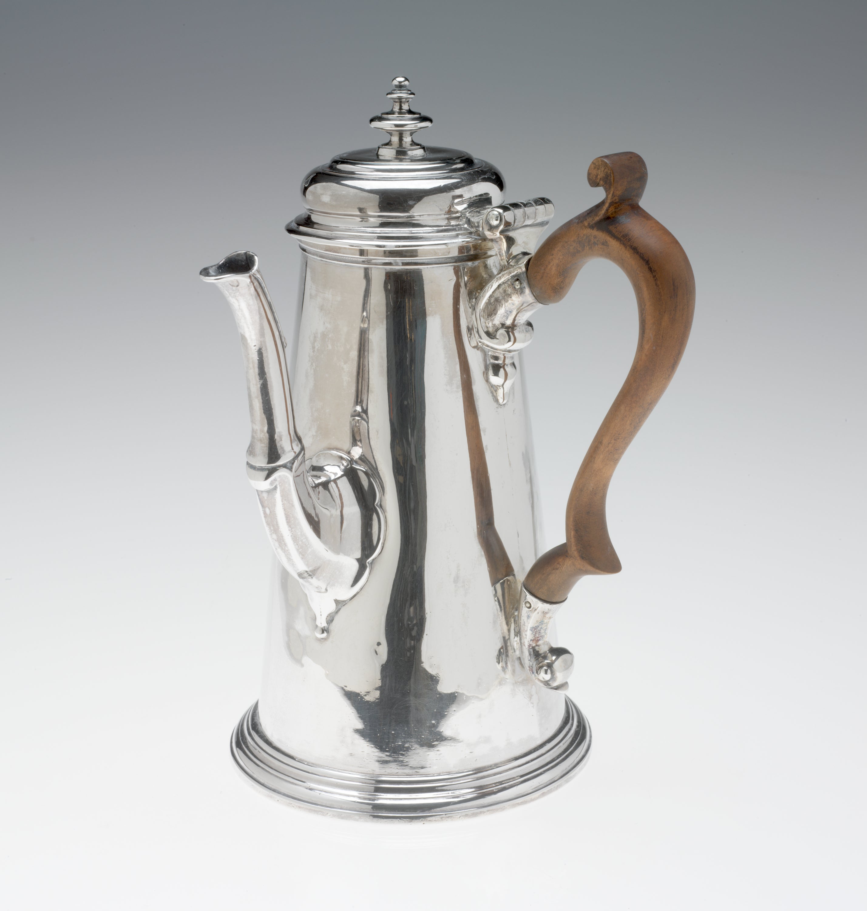 /A%20silver%20chocolate%20pot%20with%20a%20spout%2C%20hinged%20lid%2C%20and%20fruitwood%20handle%20that%20is%2090%20degrees%20from%20the%20spout.