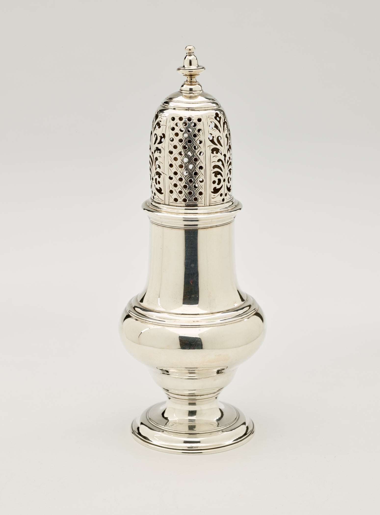 /A%20silver%20muffineer%20with%20a%20foot%2C%20rounded%20body%20that%20goes%20to%20a%20cylindrical%20top%20half%2C%20and%20the%20lid%20is%20perforated%20with%20small%20holes%20and%20floral%20cutouts.%20