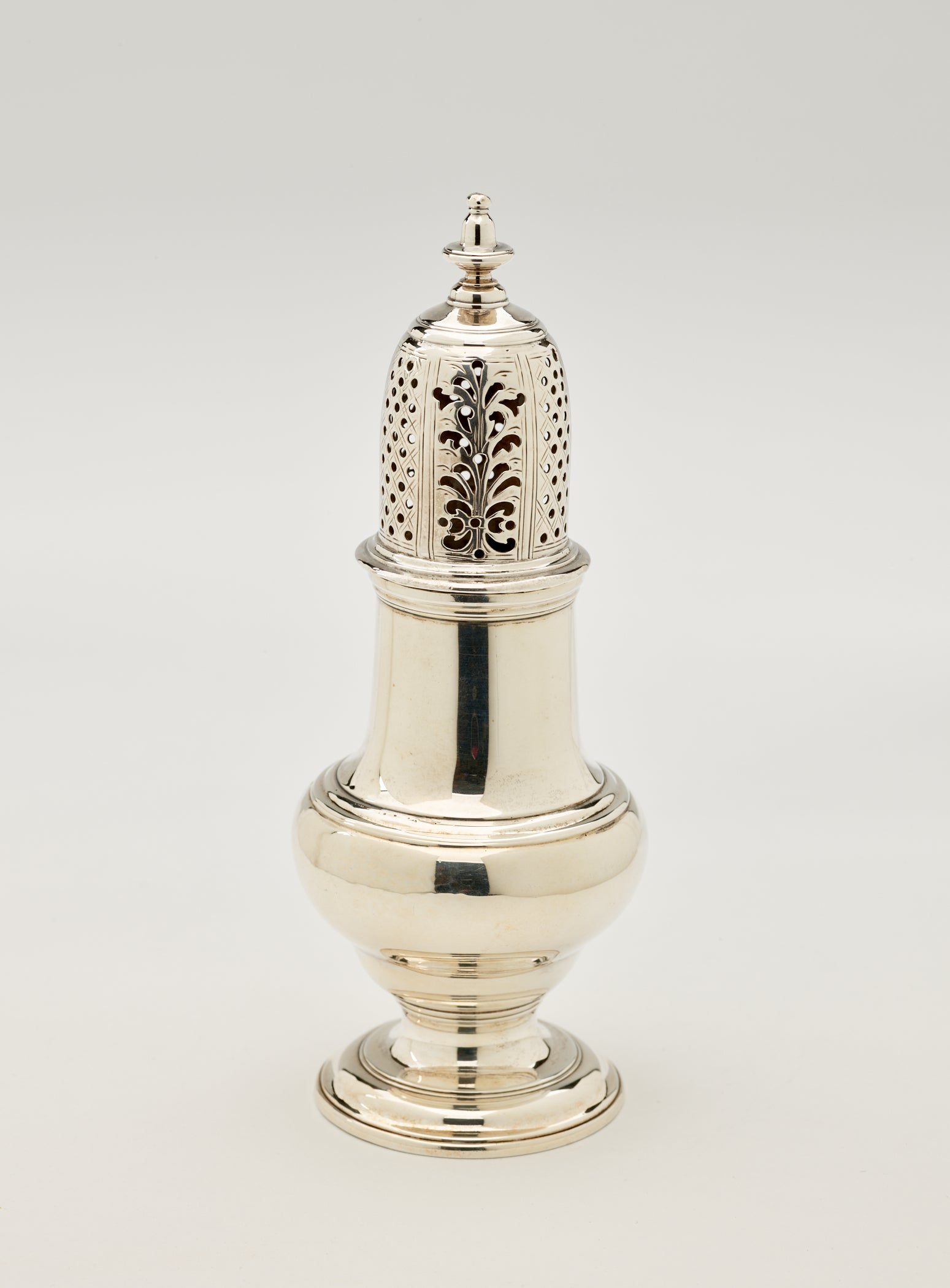 /A%20silver%20muffineer%20with%20a%20foot%2C%20rounded%20body%20that%20goes%20to%20a%20cylindrical%20top%20half%2C%20and%20the%20lid%20is%20perforated%20with%20small%20holes%20and%20floral%20cutouts.