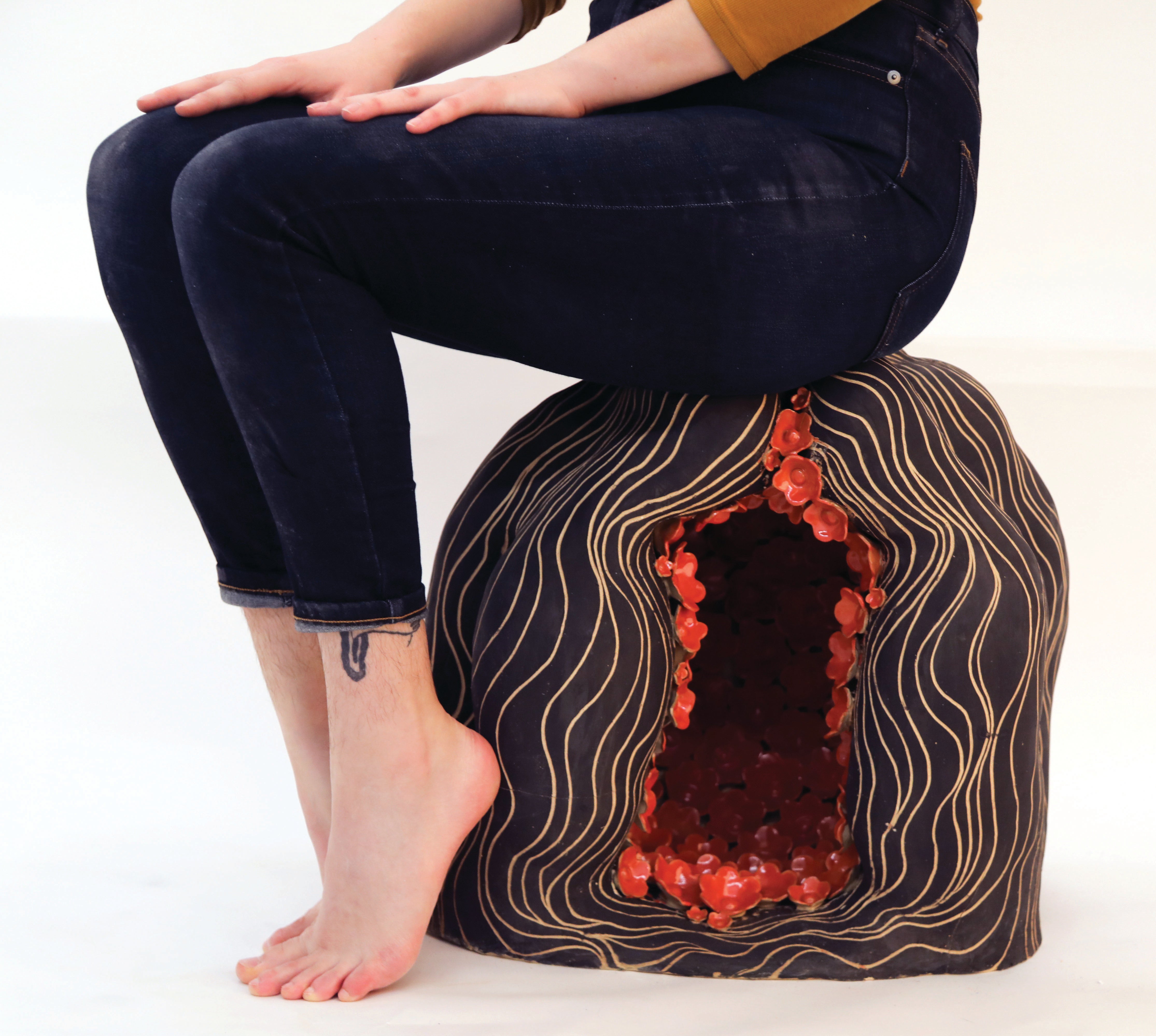 Image of a person from the waist down sitting on a ceramic head with red flowers inside its cavity.
