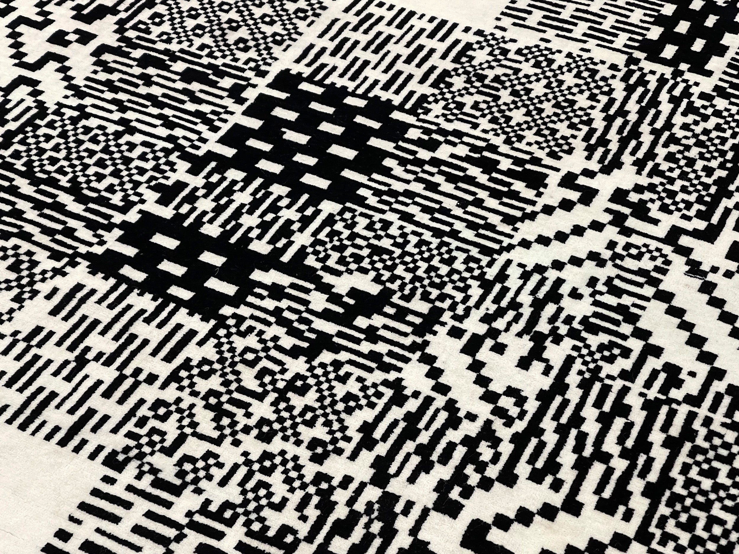 Detail documentation photograph of hand-knotted wool rug. The rug is covered in a semi-repetitive black and white patterned square image.