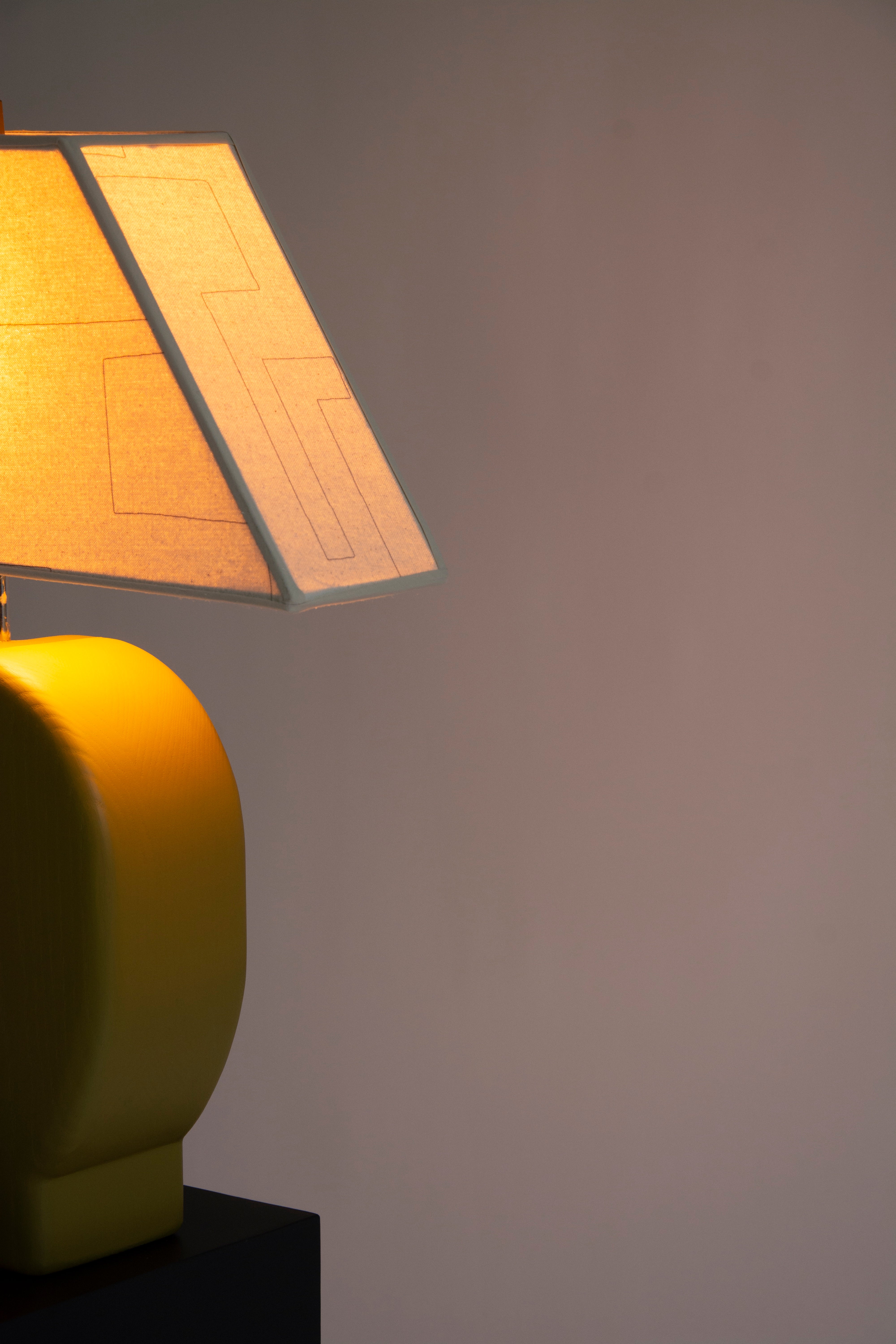 Detail view of Sister Lamp turned on, with an orange glow coming through the canvas shade.