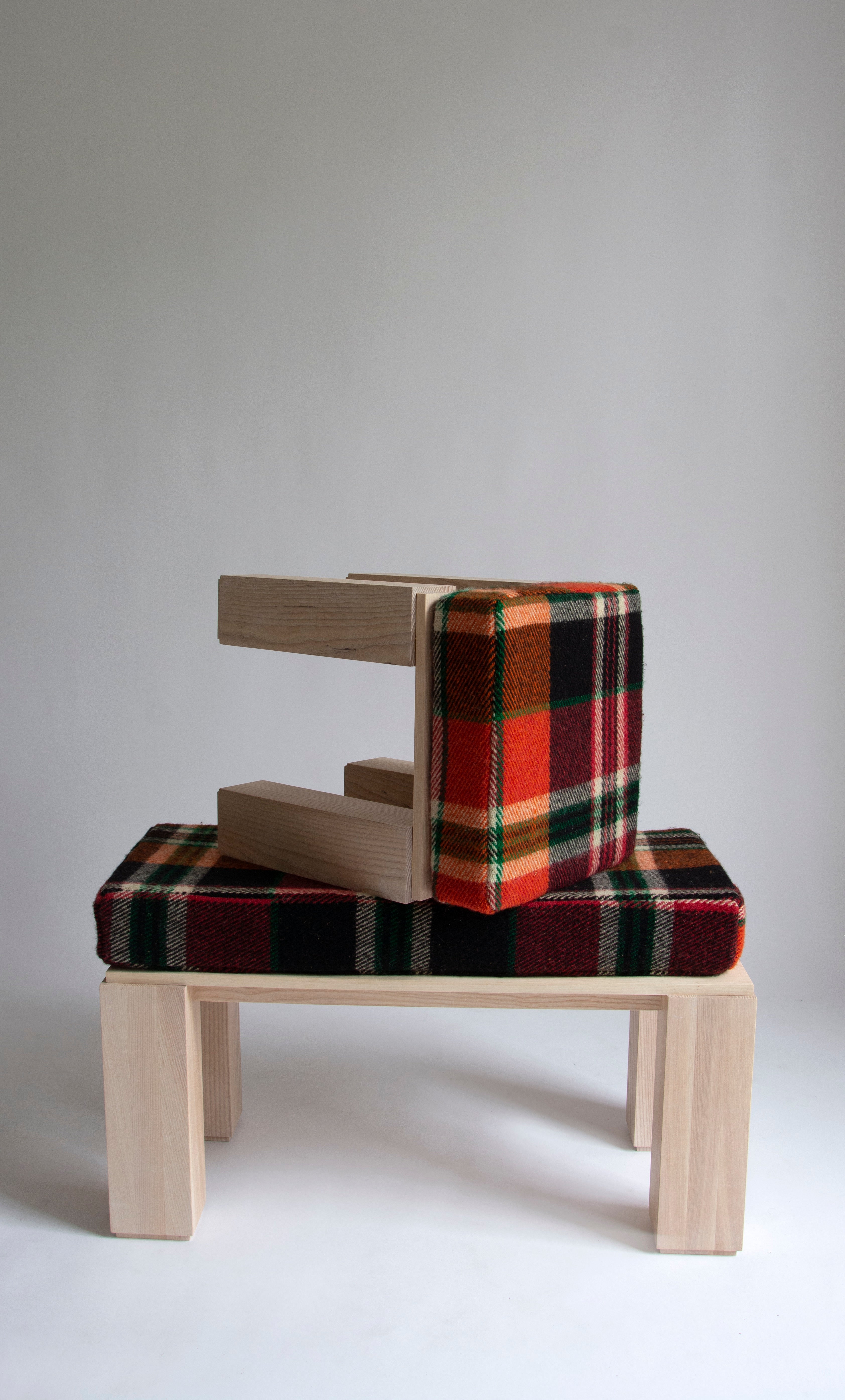 Wooden stool with orange, green and red plaid wool cushion sits kneeled on top of wooden bench with same plaid cushion.  