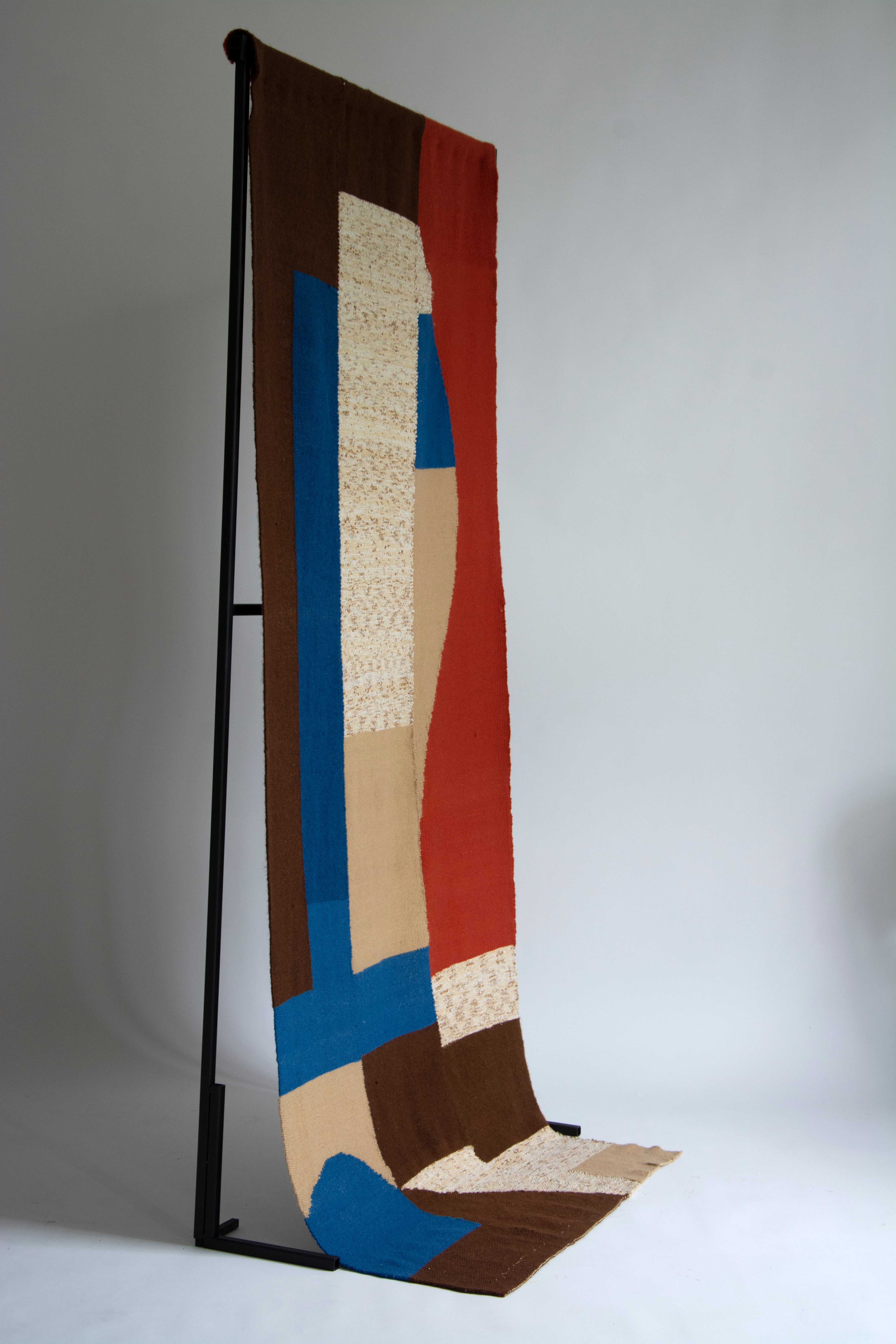 A woven tapestry, made of abstracted cobalt, vermillion, brown and beige shapes.