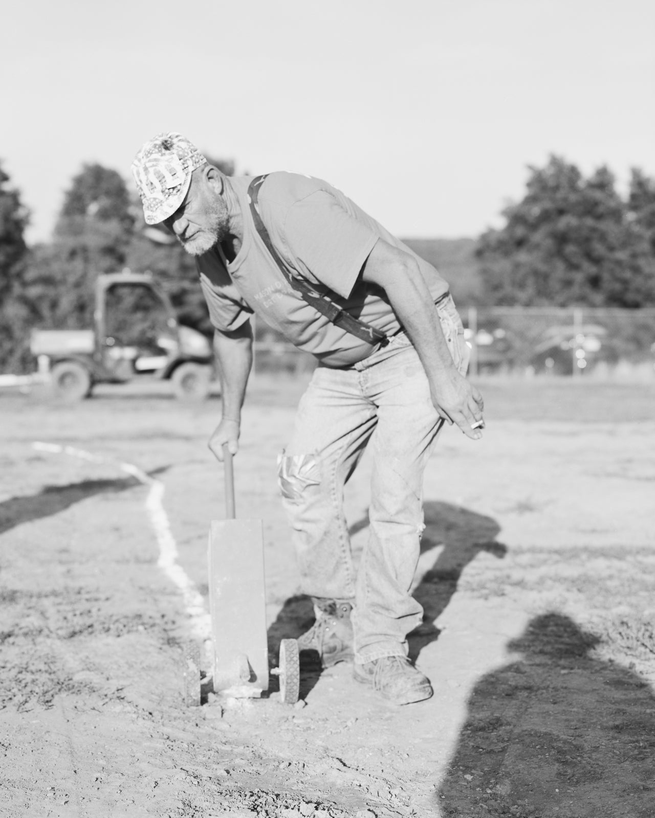 A man in the bright sun drags a chalk line behind him.