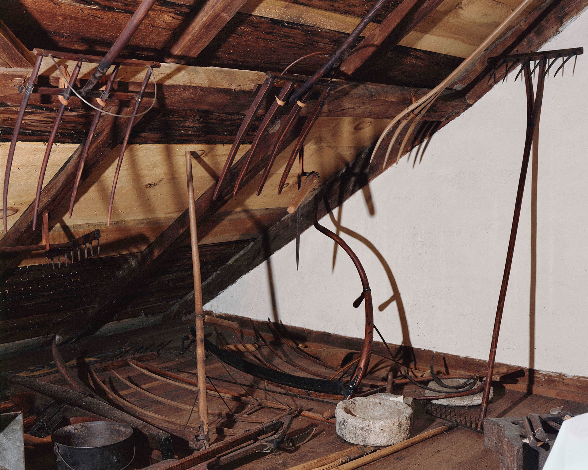 Photograph of various farmings tools hung in a dark attic.