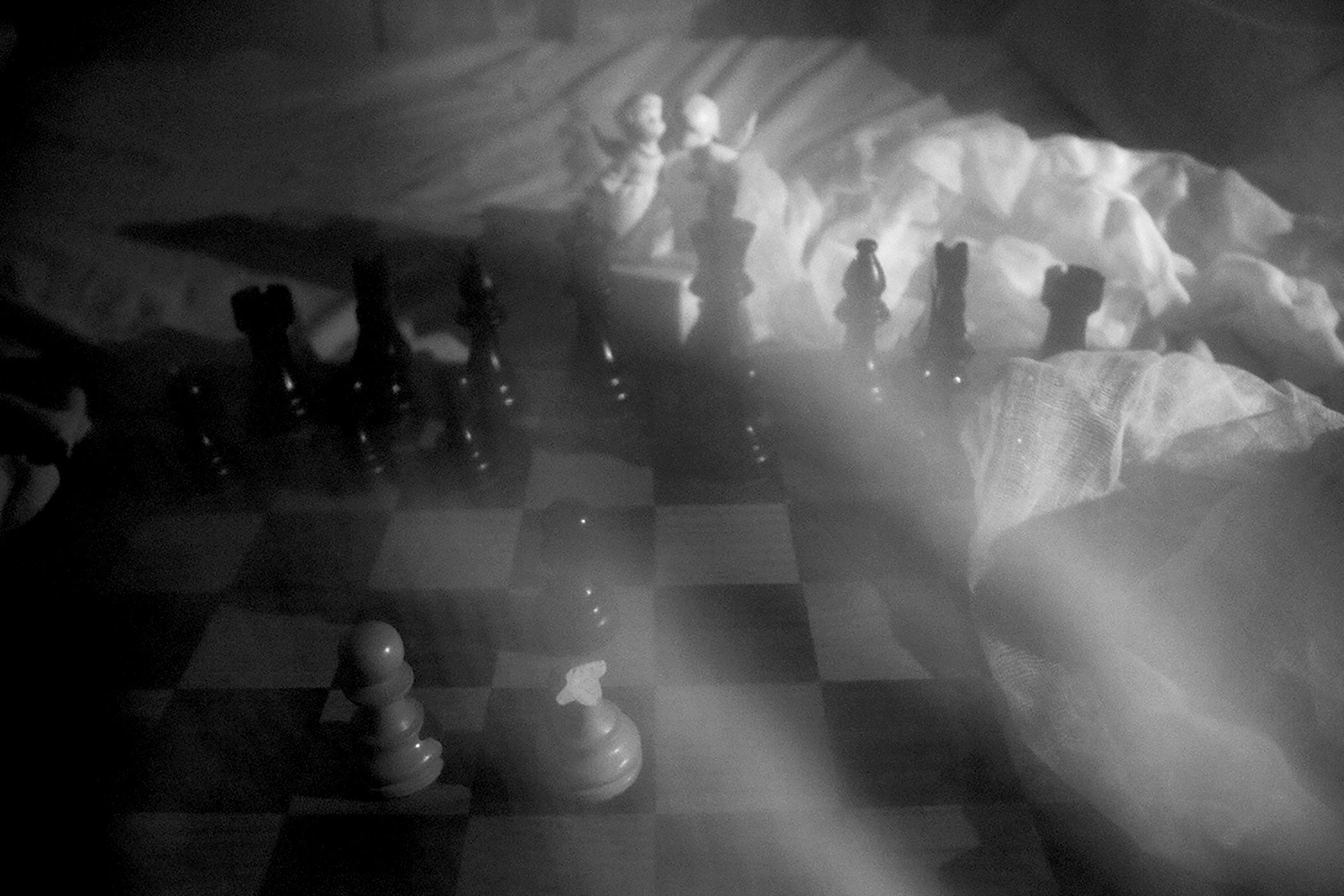 Chess board sitting on top of bed sheets a long with two porcelain angels in the background. 