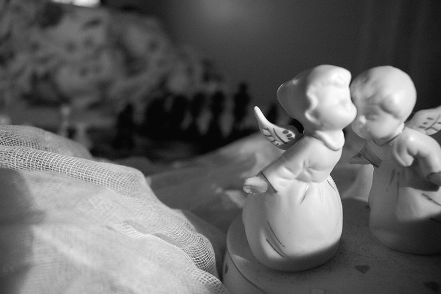 Chess board sitting on top of bed sheets a long with two porcelain angels in the foreground.