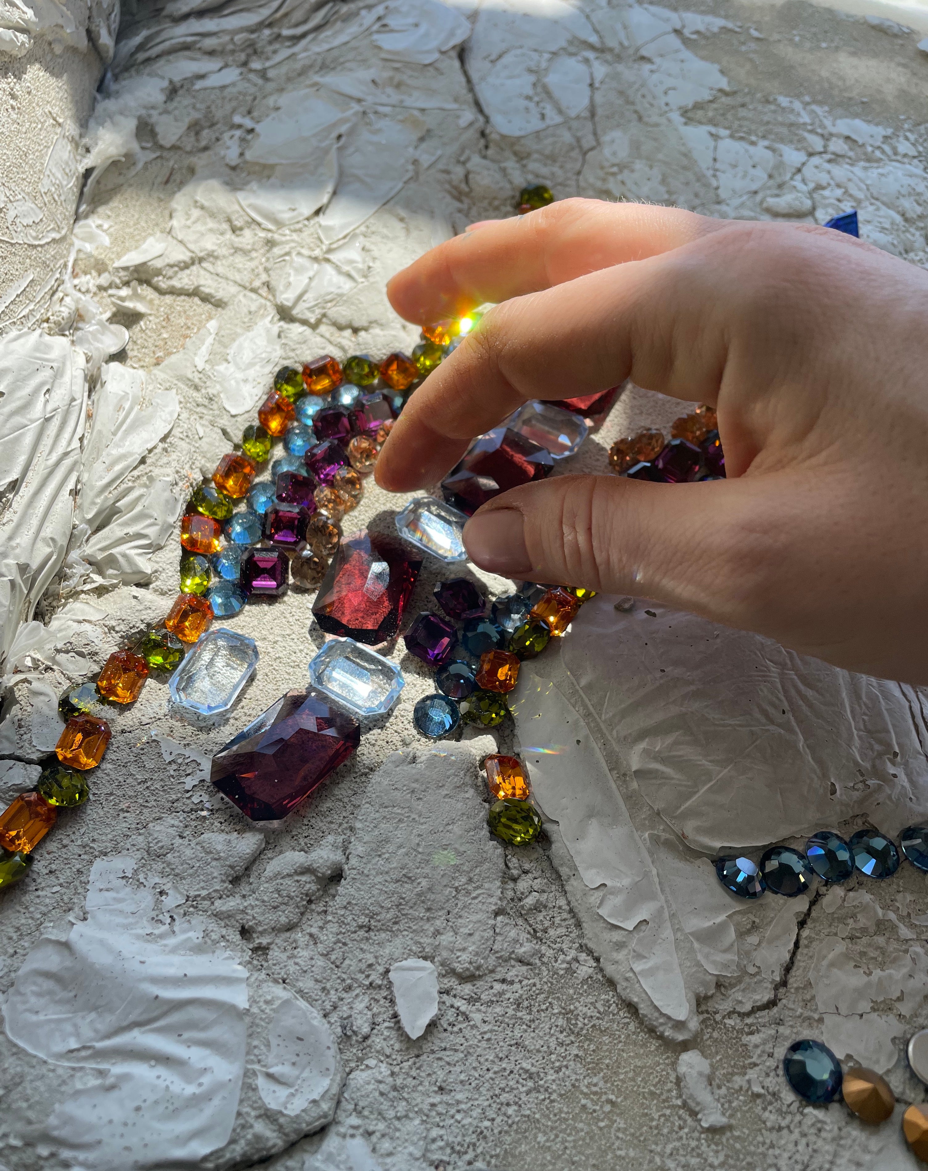 Sunlight piercing various colors of crystals casts rainbows onto a hand.