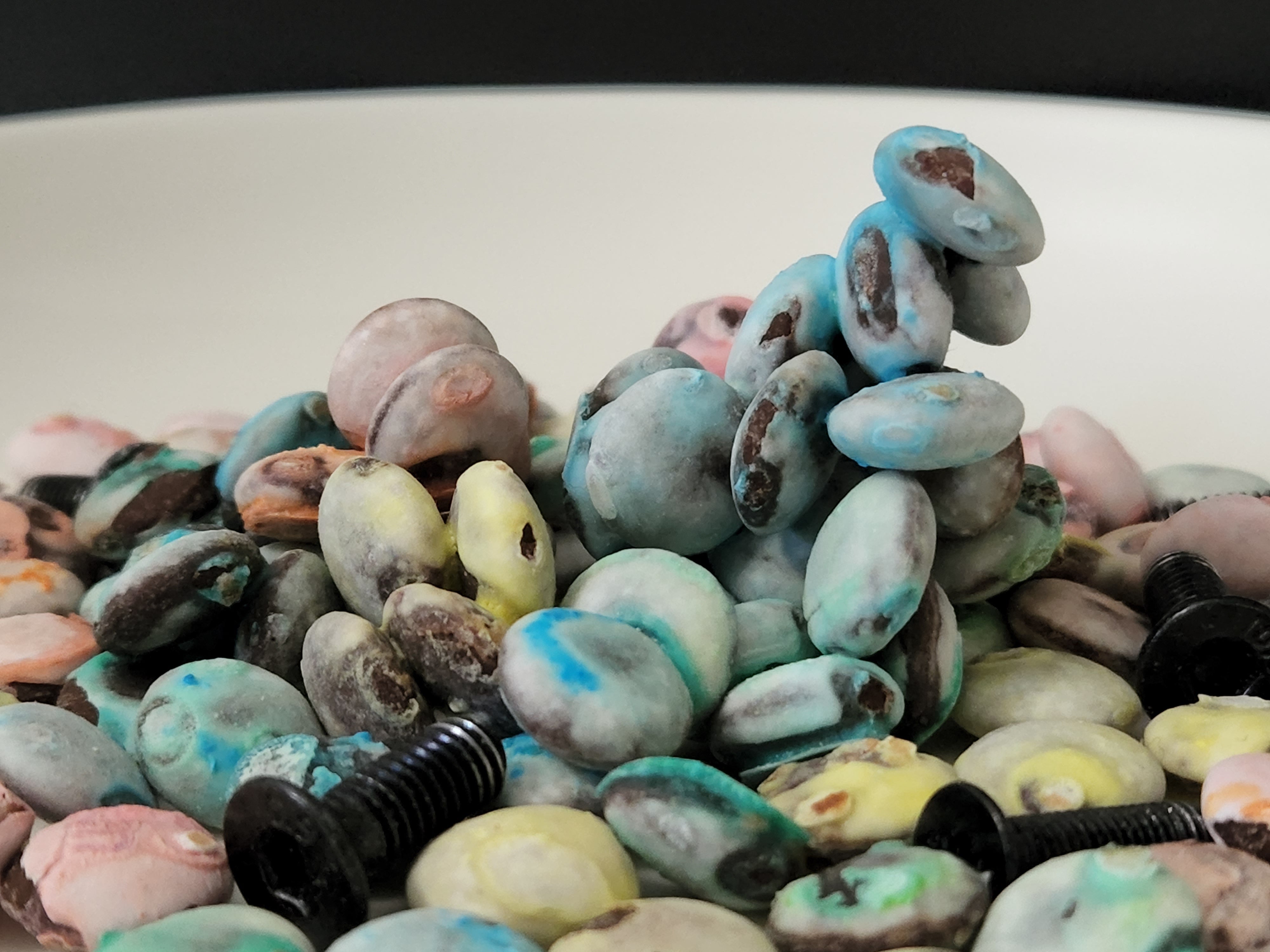 Discolored M&Ms candies on a white ceramic plate, together with screws