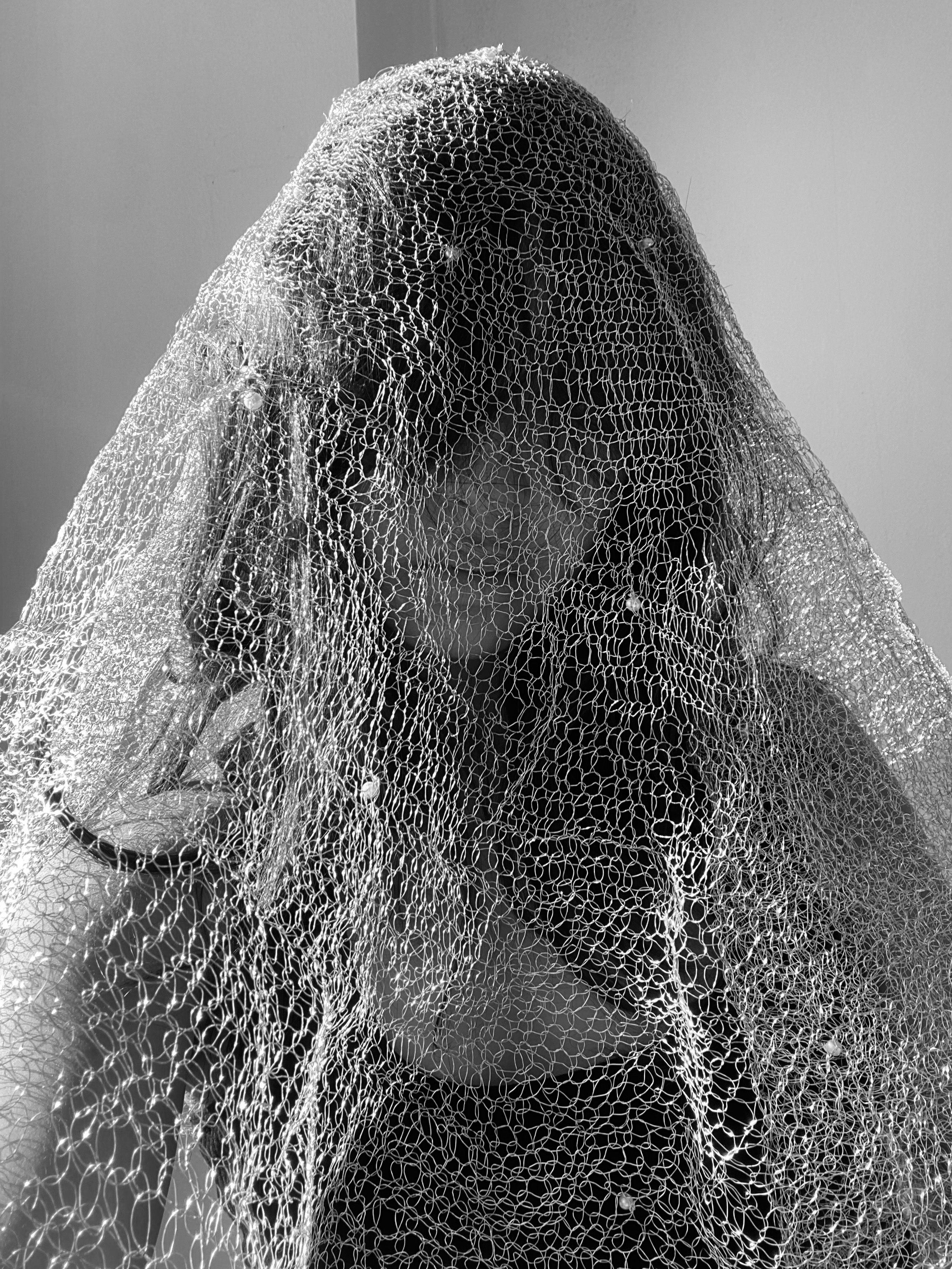 There is a girl wearing a metal veil with pearls to obscure her face.