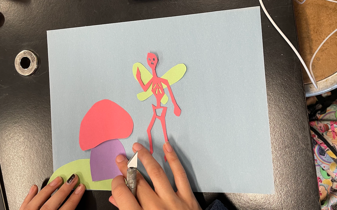 A student glues down her cut out shape onto a piece of construction paper. 