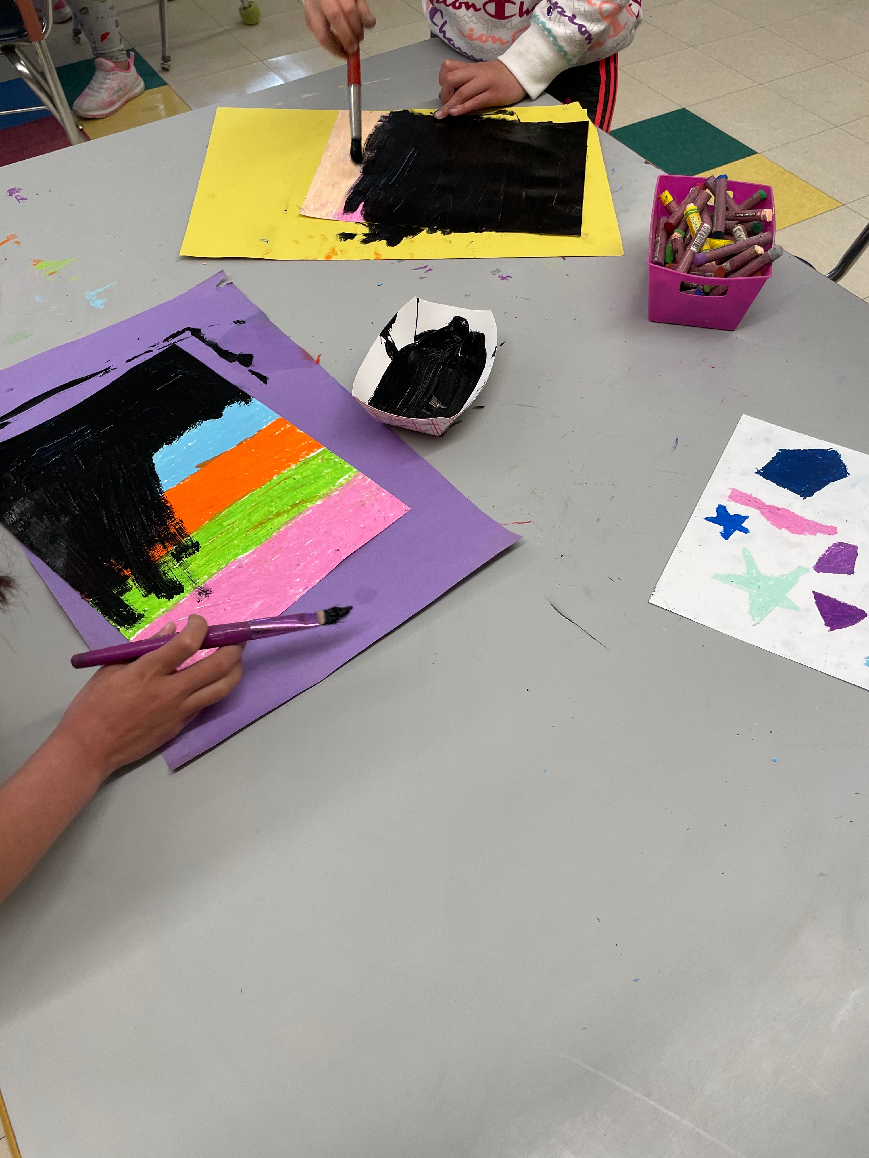 Students cover oil pastel colors with tempera paint to prepare for etching. 