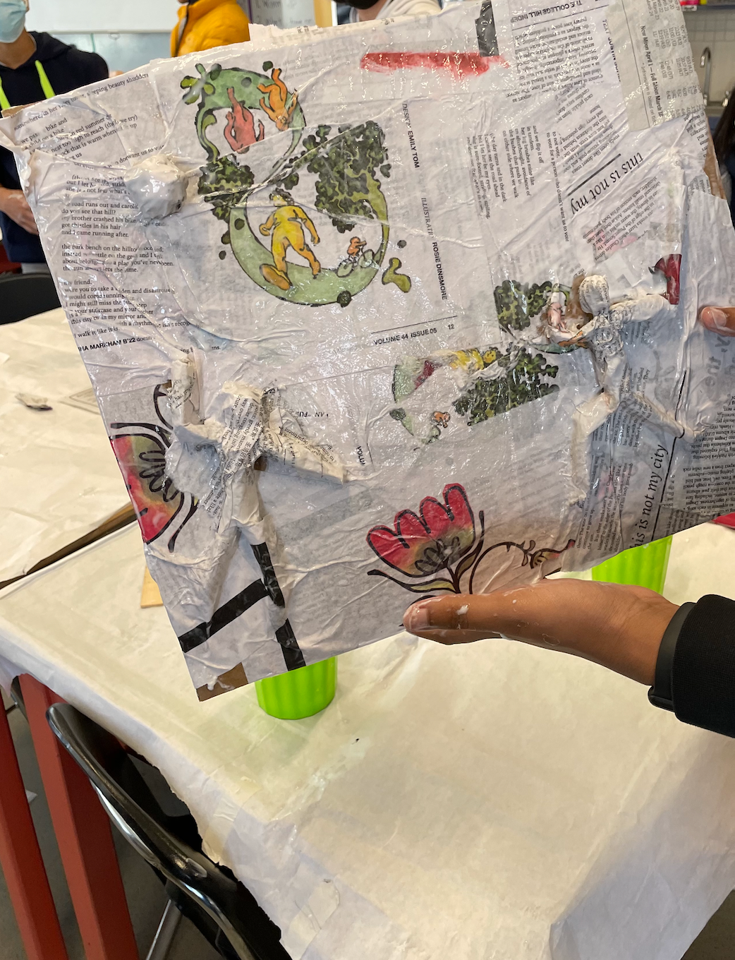 This is a photo of students applying paper maché to their masking tape bases and working together to help a friend!