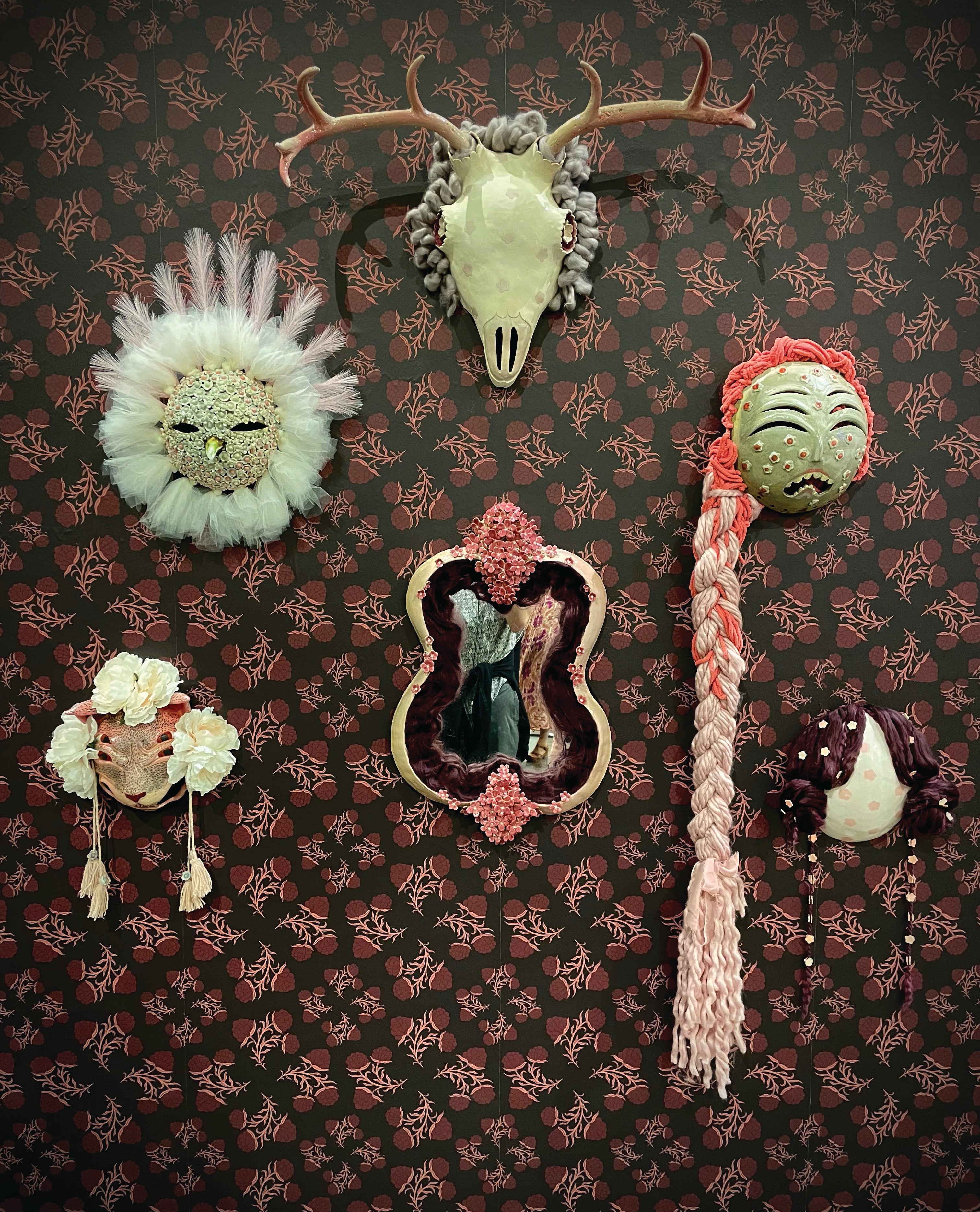 Ceramic masks hang on a wall covered in burgundy floral wallpaper.