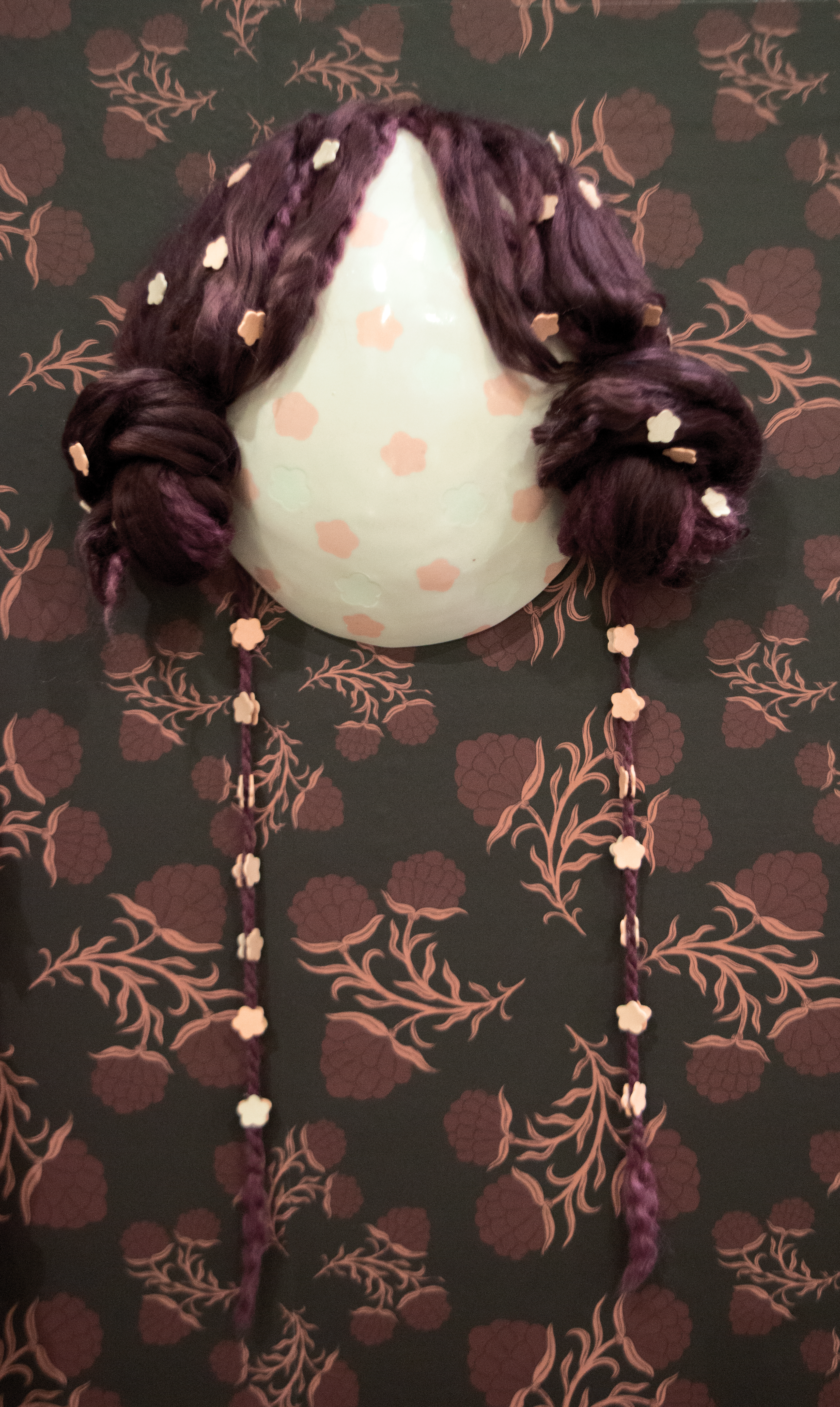 White and pink ceramic mask with yarn hair buns covered in small pink flowers. 
