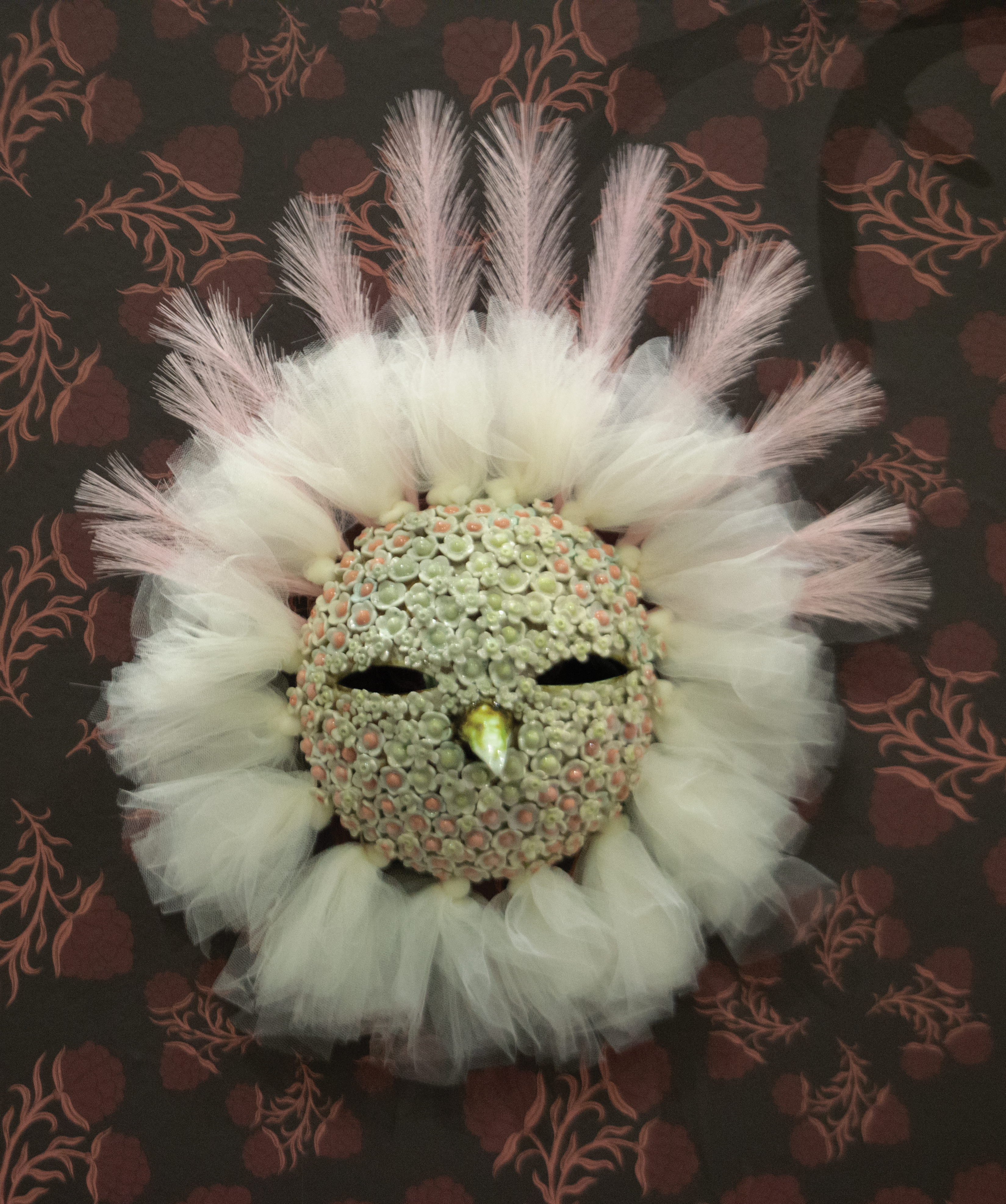 Ceramic bird mask covered in ceramic flowers, ringed in white tulle. 